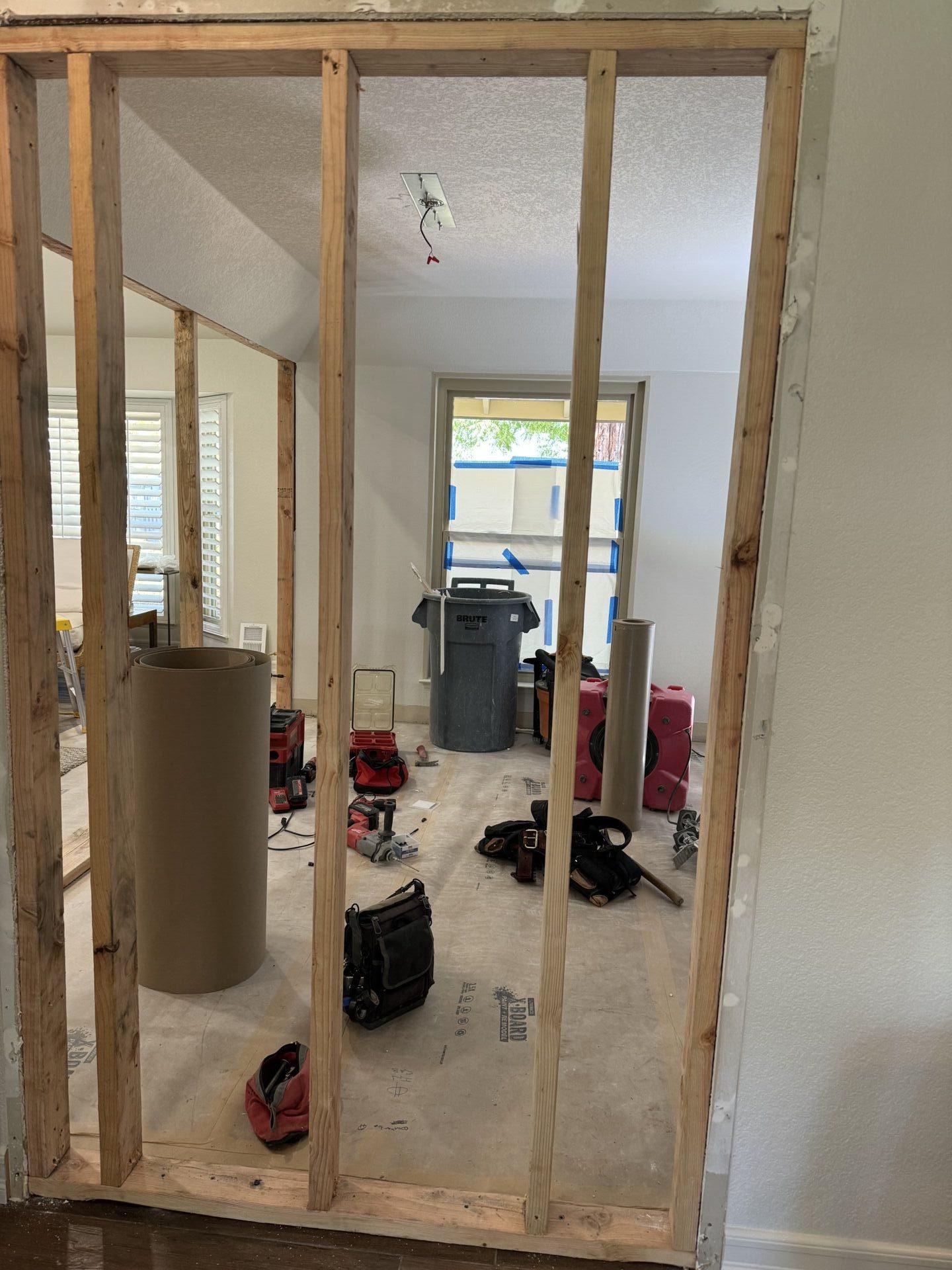 Wood wall framing takes shape during the conversion of an open dining room into an enclosed home office. The construction photograph shows the new wall studs, exposed interior, and protected flooring.
