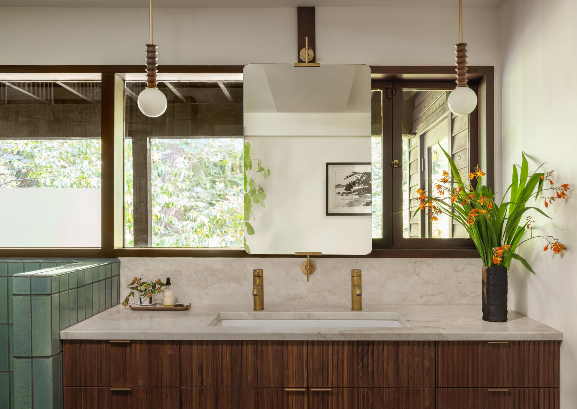 Explore the primary ensuite bathroom of The Burrows, a renovated mid-century home in Seattle by chadbourne + doss architects. Green Heath tiles, a freestanding soaking tub, brass fixtures, and a custom walnut double vanity create a beautiful modern bathroom.