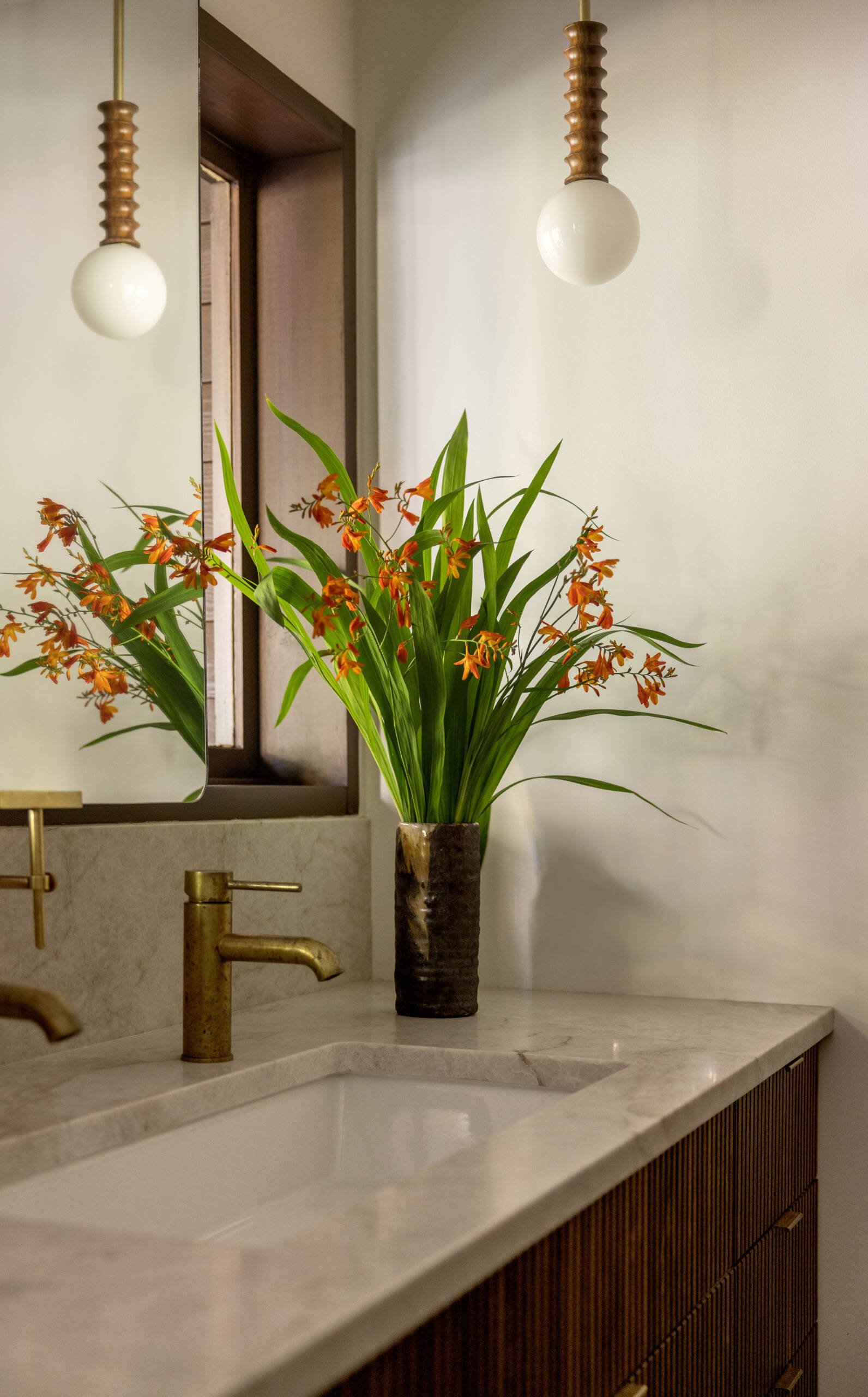 Explore the primary ensuite bathroom of The Burrows, a renovated mid-century home in Seattle by chadbourne + doss architects. Green Heath tiles, a freestanding soaking tub, brass fixtures, and a custom walnut double vanity create a beautiful modern bathroom.