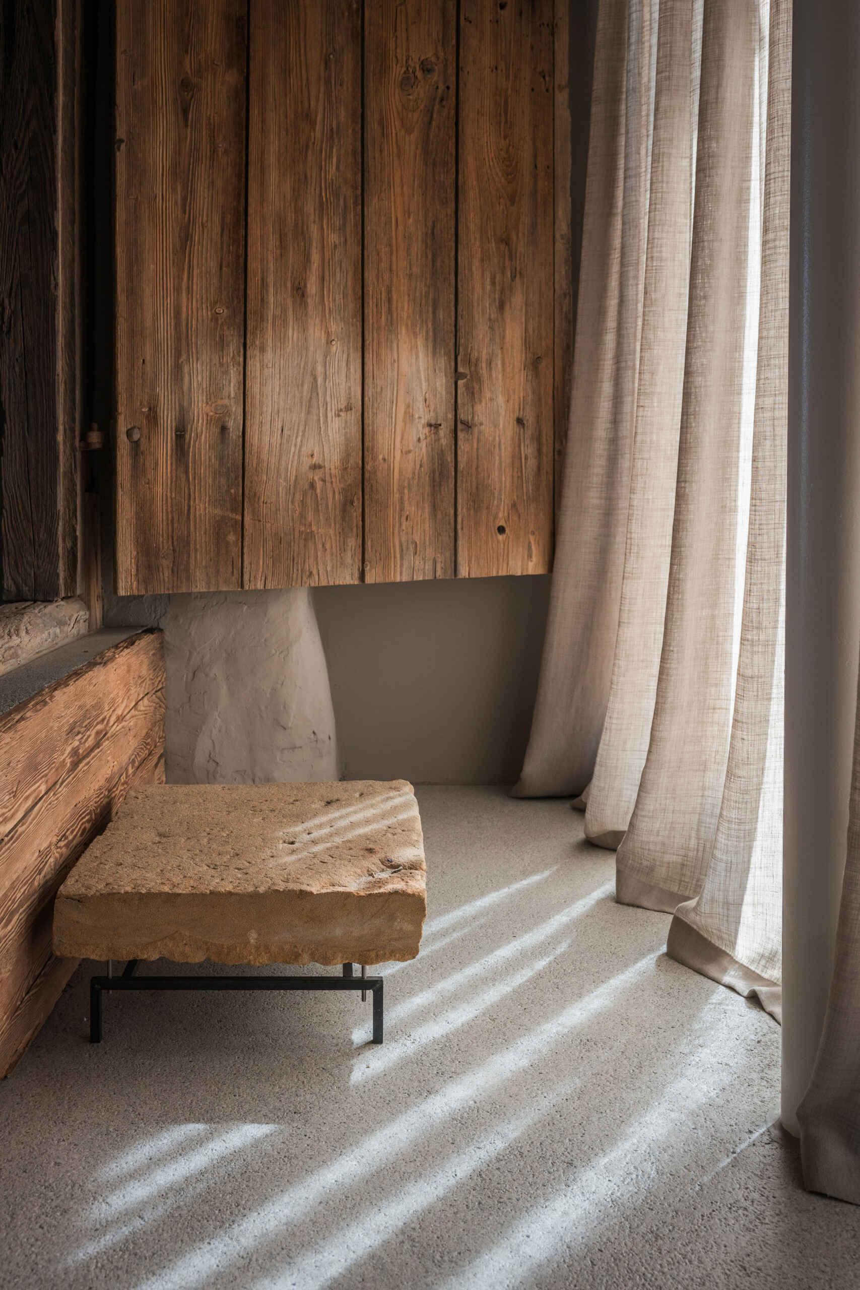An Austrian farmhouse entryway combines weathered timber, a stone bench, linen curtains, and a modern interior with unusual architectural details.