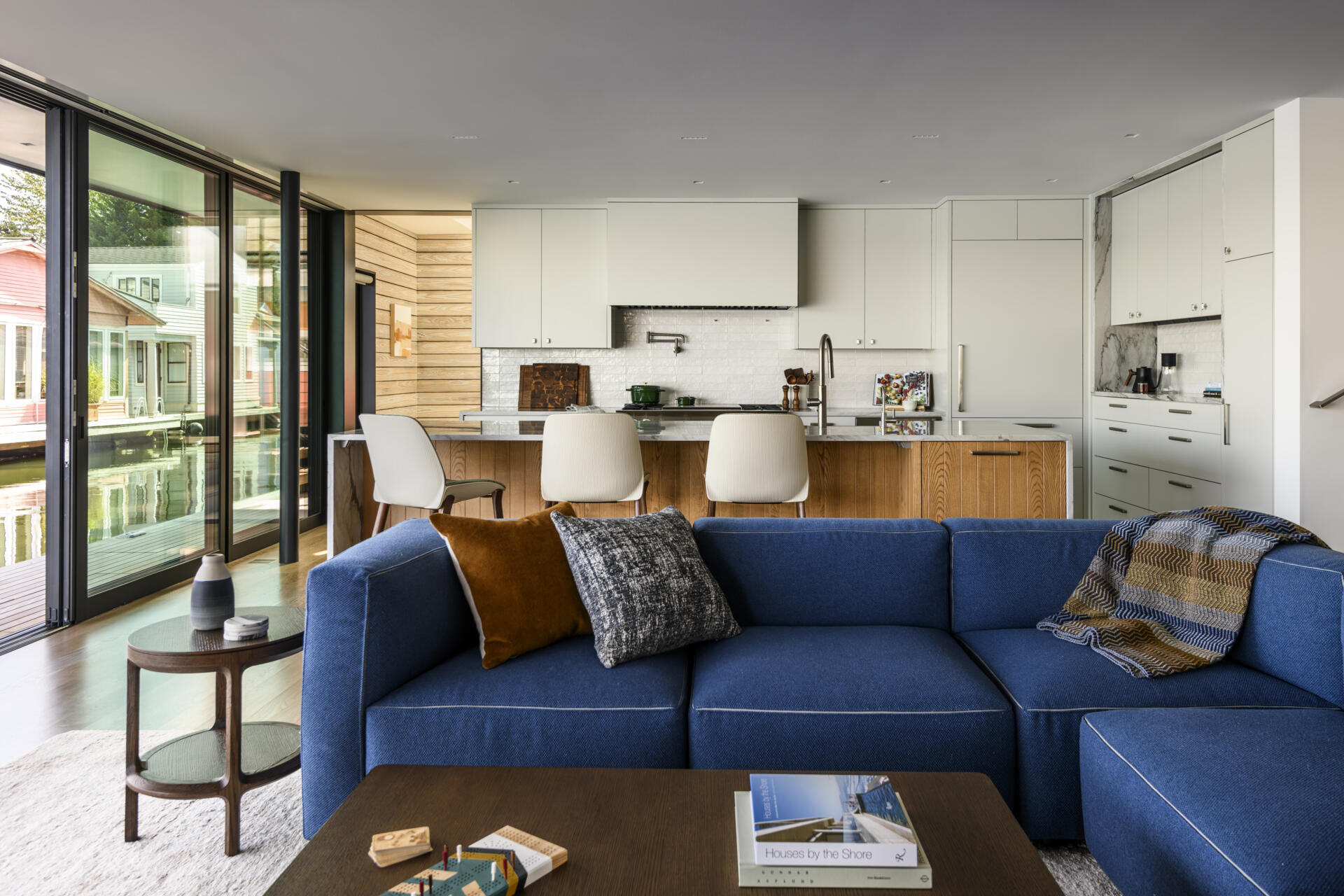 Featuring white cabinets, a marble-look waterfall island, warm wood accents, a BlueStar range, and upholstered counter stools, this bright kitchen combines coastal style with practical family living.