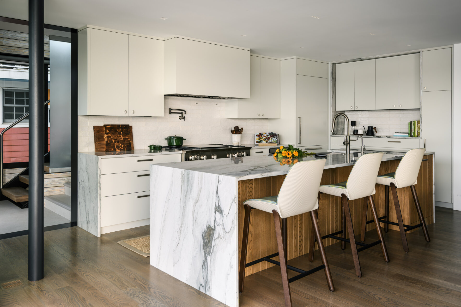 Featuring white cabinets, a marble-look waterfall island, warm wood accents, a BlueStar range, and upholstered counter stools, this bright kitchen combines coastal style with practical family living.