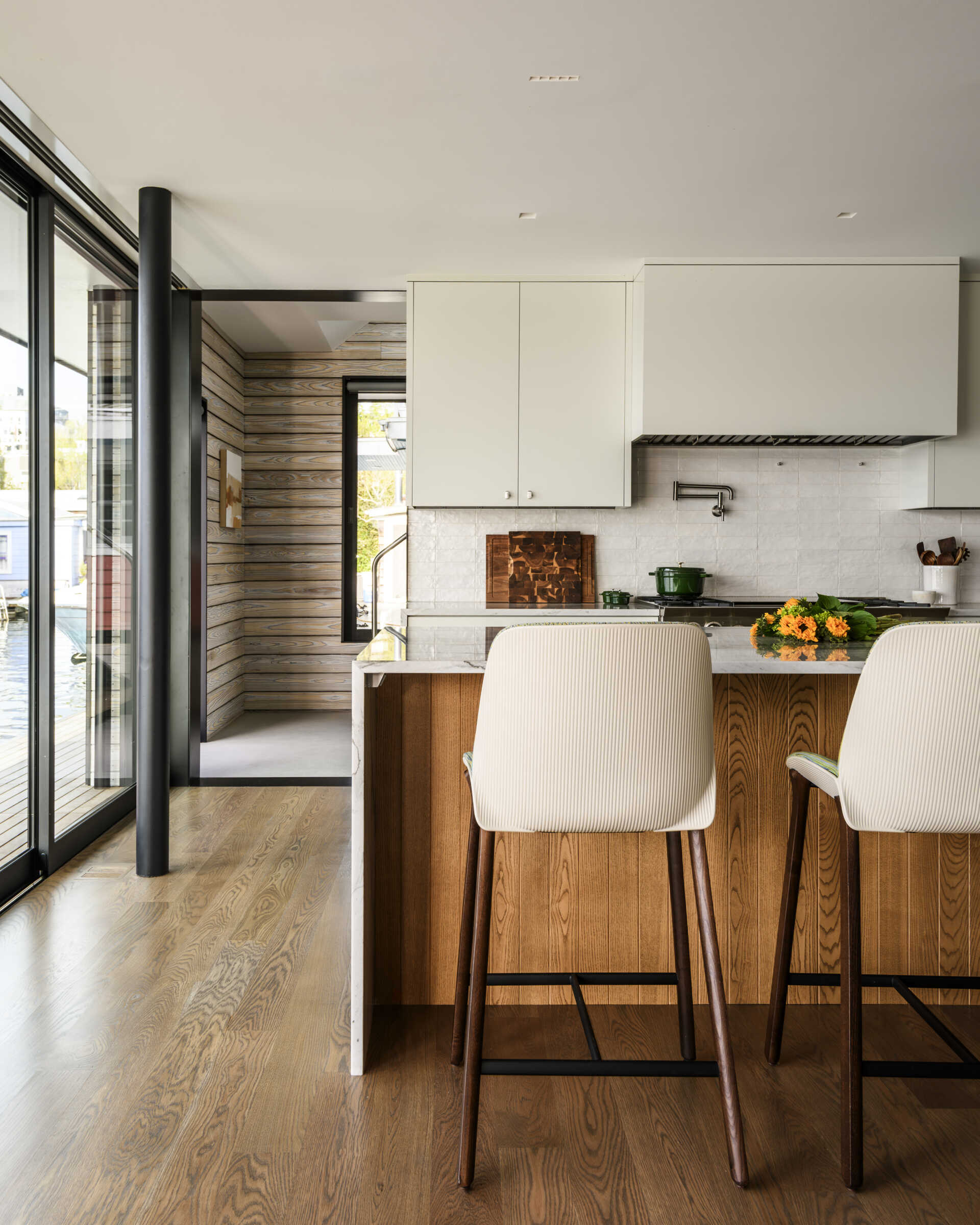Featuring white cabinets, a marble-look waterfall island, warm wood accents, a BlueStar range, and upholstered counter stools, this bright kitchen combines coastal style with practical family living.