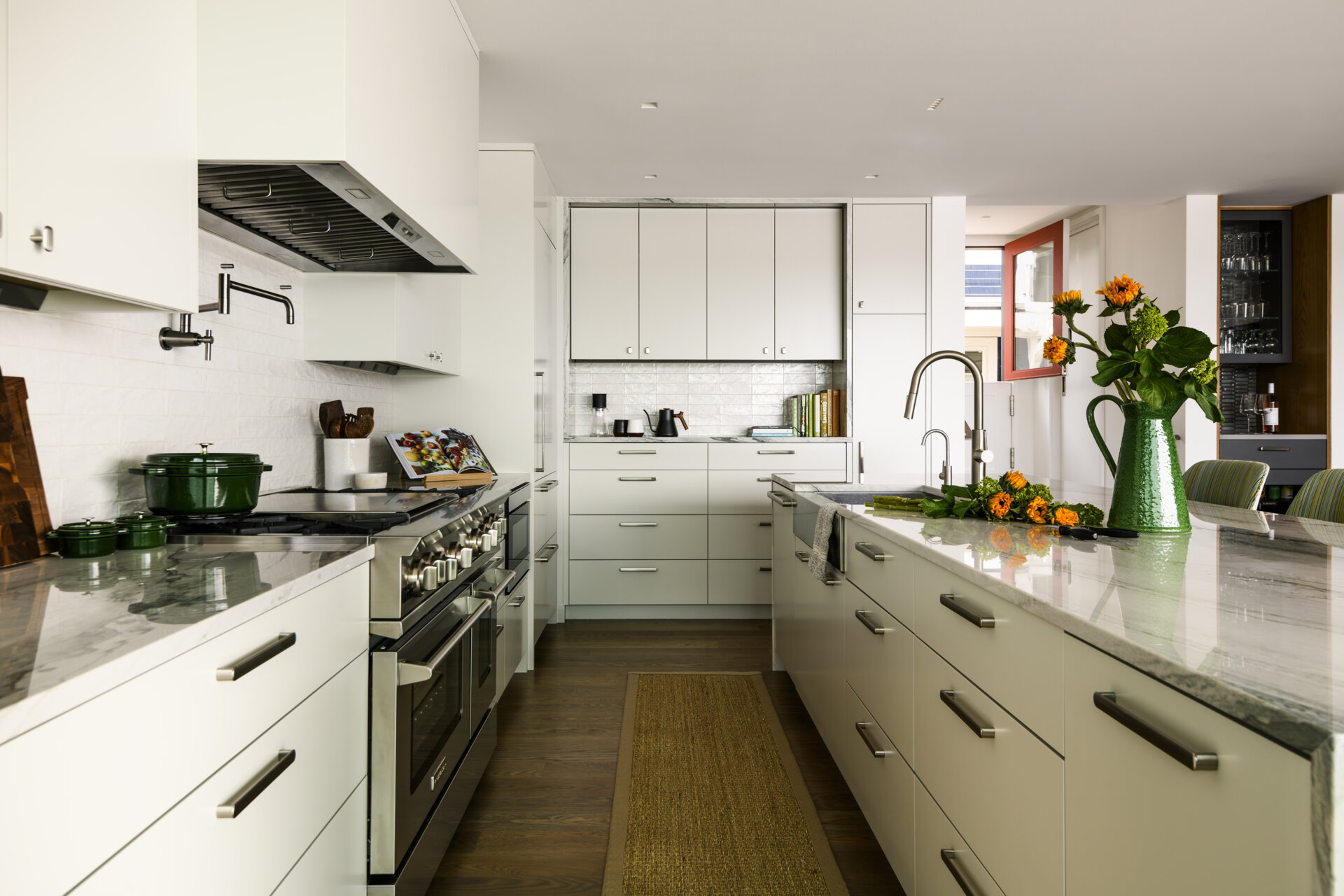 Featuring white cabinets, a marble-look waterfall island, warm wood accents, a BlueStar range, and upholstered counter stools, this bright kitchen combines coastal style with practical family living.