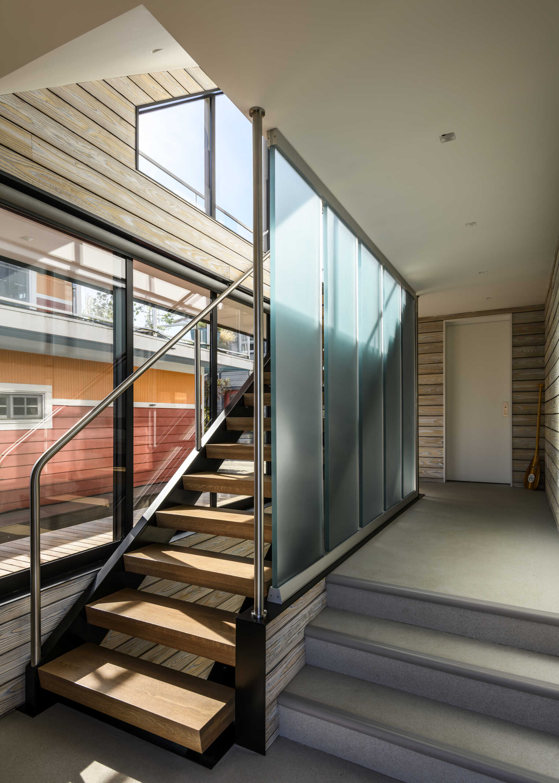 Open wood stairs, custom metal railings, translucent resin panels, weathered wood siding, and a skylit hallway bring modern and nautical design details together.