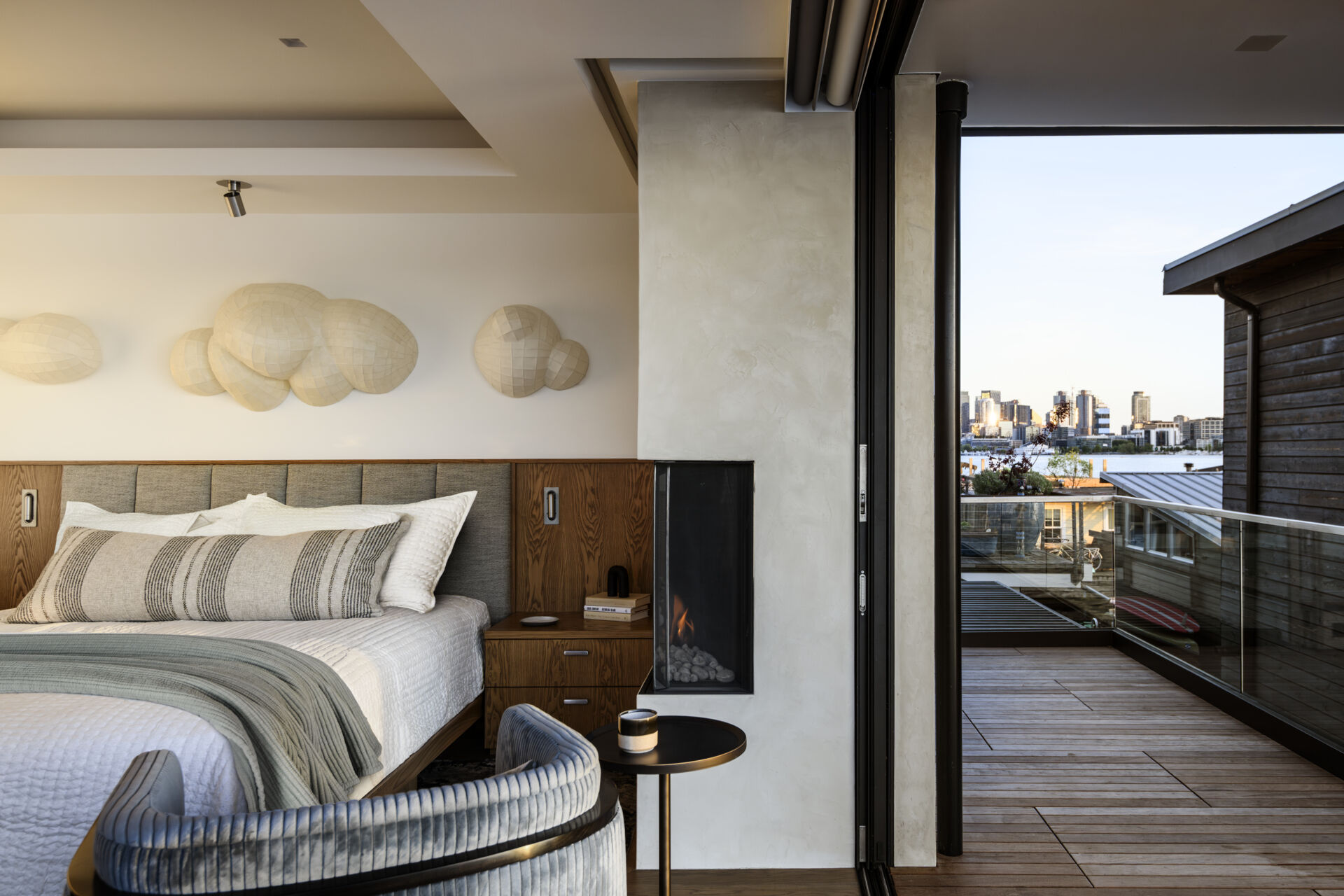 Featuring a private waterfront balcony, corner fireplace, upholstered headboard, built-in wood cabinetry, and soft coastal colors, this modern bedroom offers beautiful lake views.