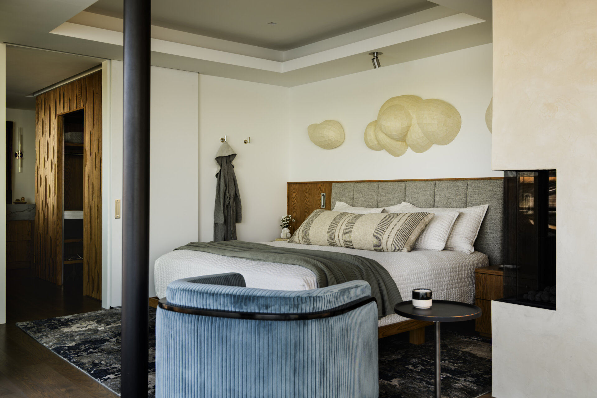 Featuring a private waterfront balcony, corner fireplace, upholstered headboard, built-in wood cabinetry, and soft coastal colors, this modern bedroom offers beautiful lake views.