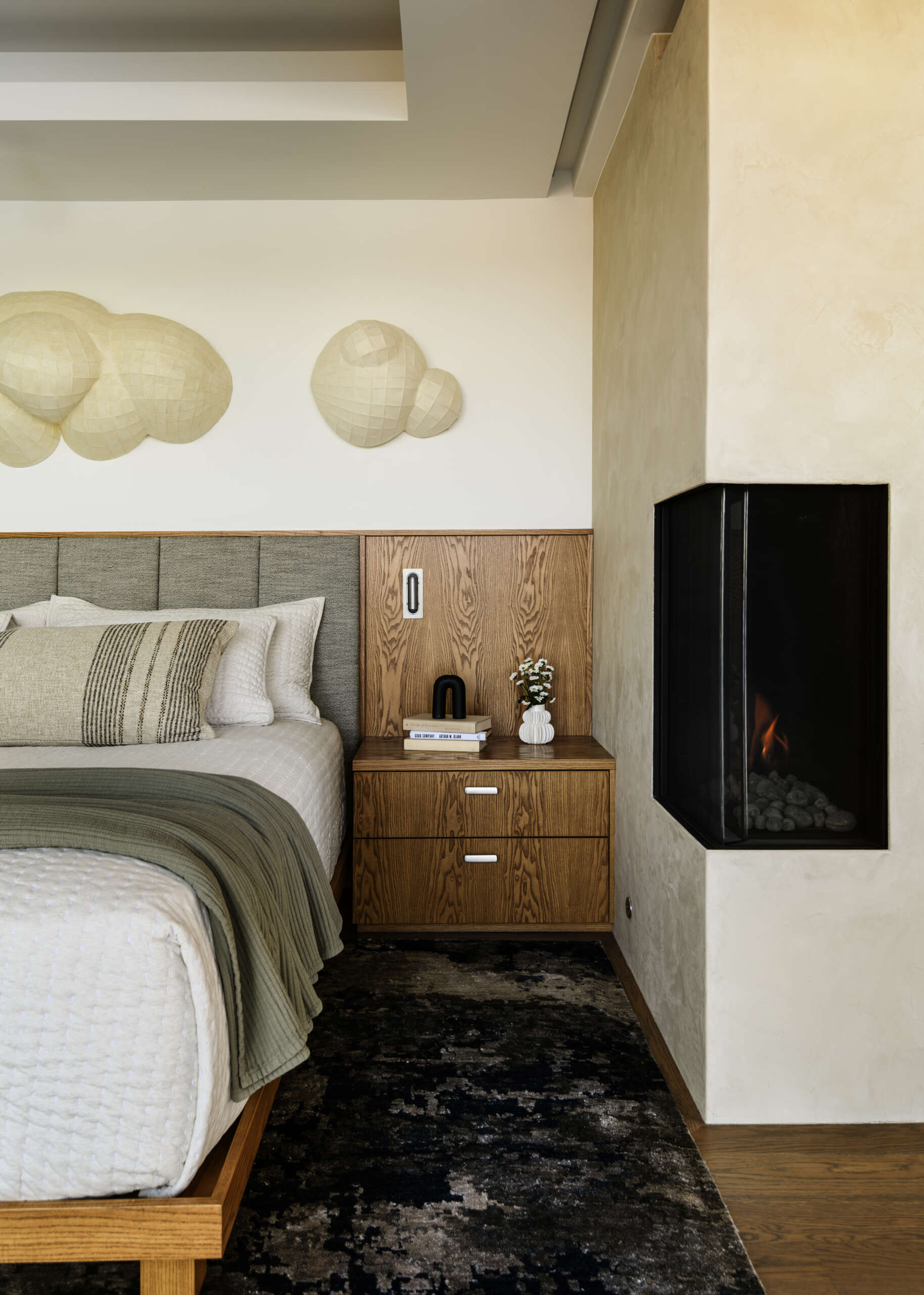 Featuring a private waterfront balcony, corner fireplace, upholstered headboard, built-in wood cabinetry, and soft coastal colors, this modern bedroom offers beautiful lake views.
