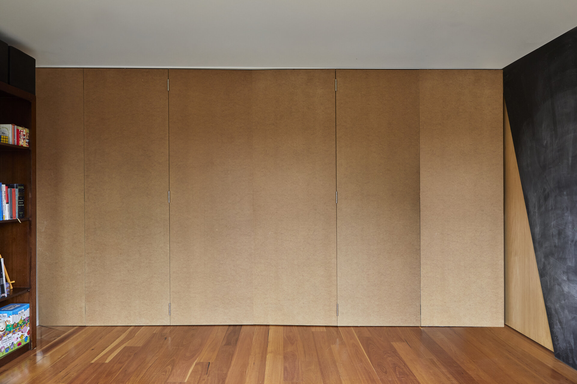 A full-height folding partition forms a continuous wall of warm brown panels, creating a flexible room divider beside a black chalkboard feature wall.