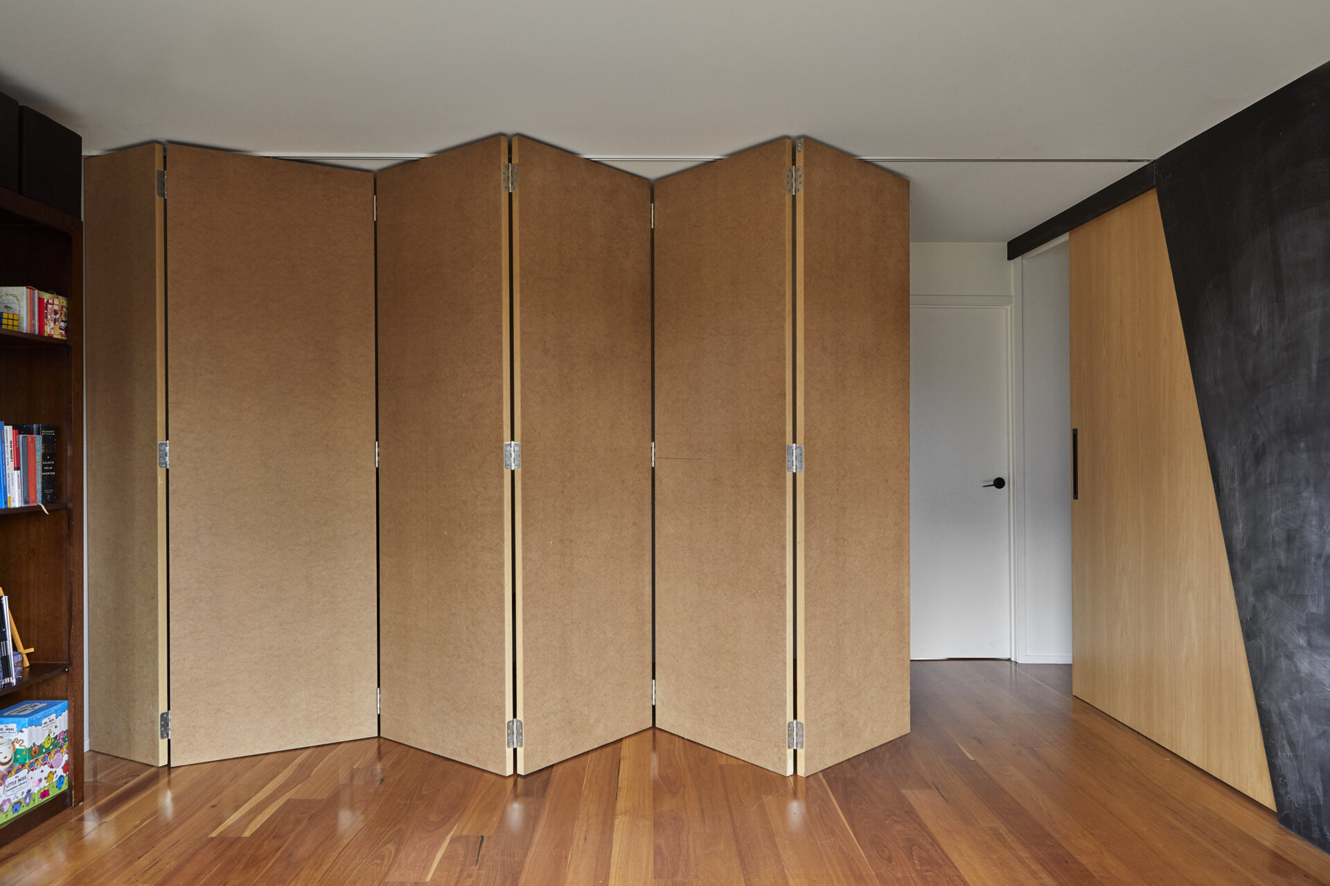 A folding room divider with hinged panels extends across a modern interior. The accordion-style partition can be folded to one side to open up the adjoining space.