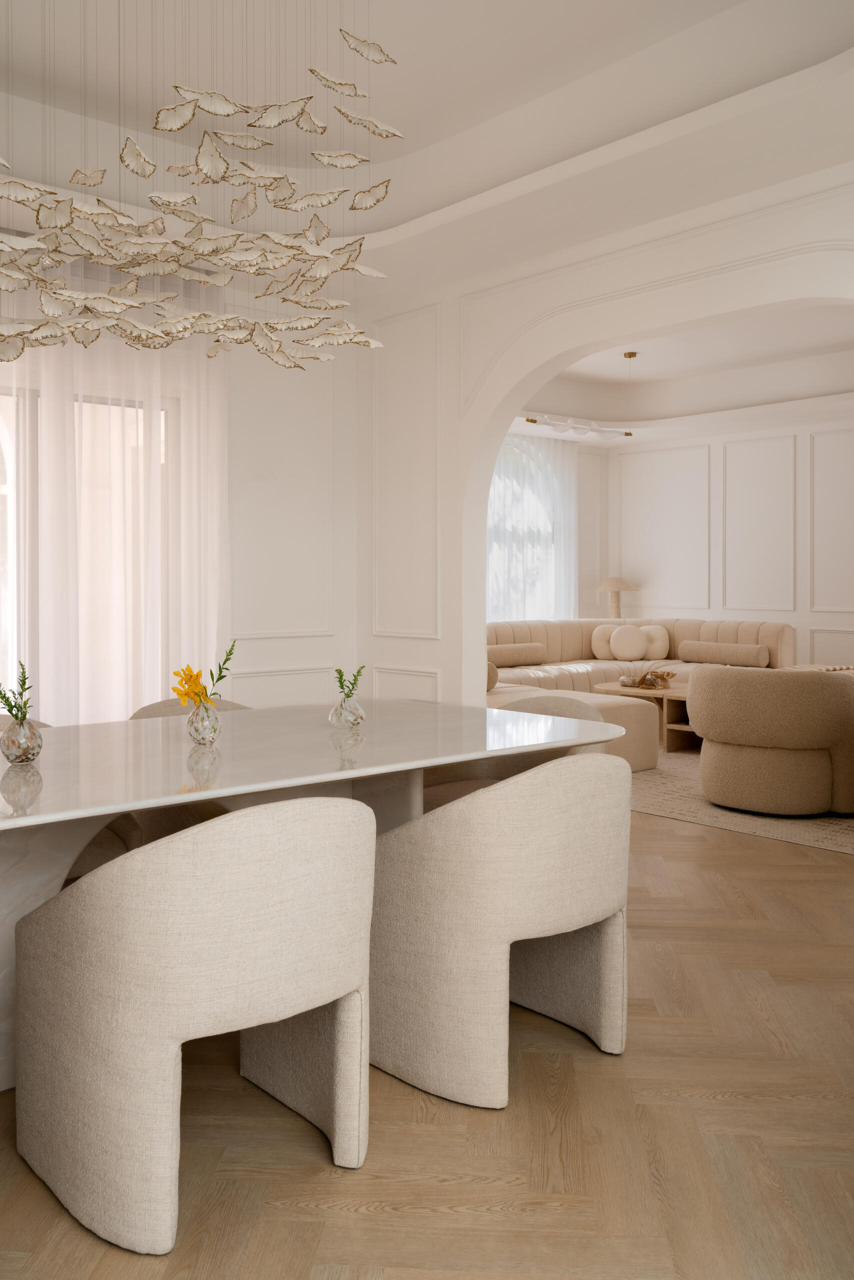 This luxurious formal dining room in Dubai features a monumental white onyx dining table by DOT Objects, sculptural arched bases, curved upholstered dining chairs, and an incredible suspended leaf installation. Designed by D’Ora Tokai Designs for The White Arcade.