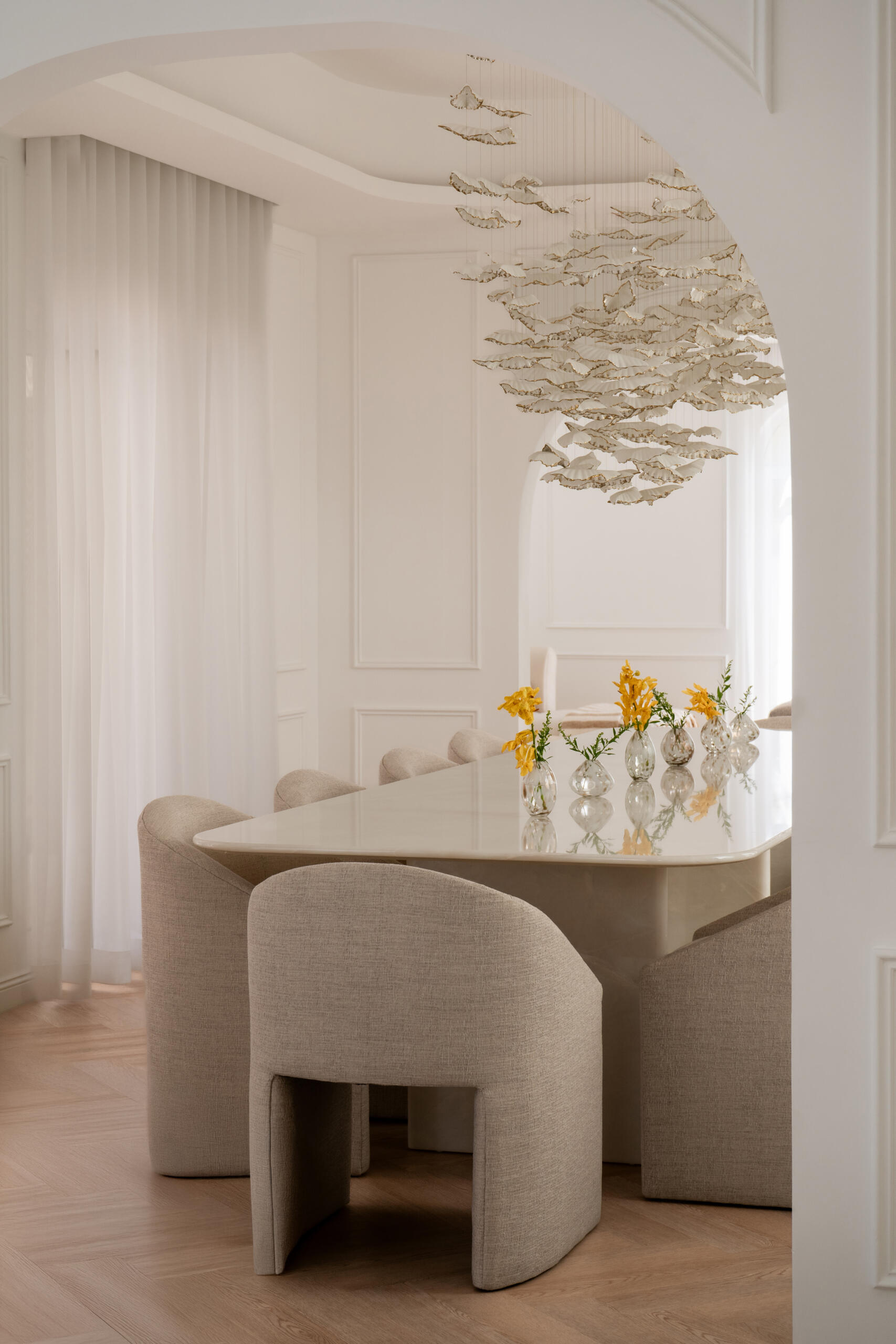 This luxurious formal dining room in Dubai features a monumental white onyx dining table by DOT Objects, sculptural arched bases, curved upholstered dining chairs, and an incredible suspended leaf installation. Designed by D’Ora Tokai Designs for The White Arcade.