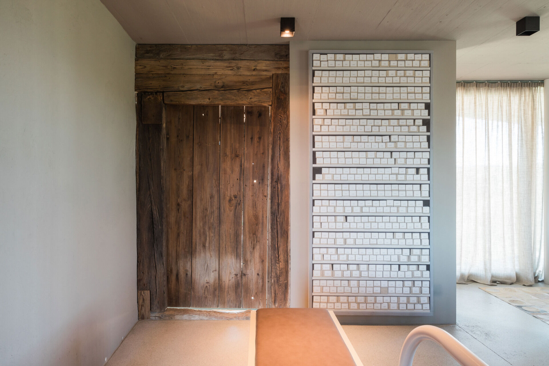 An Austrian farmhouse entryway combines weathered timber, a stone bench, linen curtains, and a modern interior with unusual architectural details.