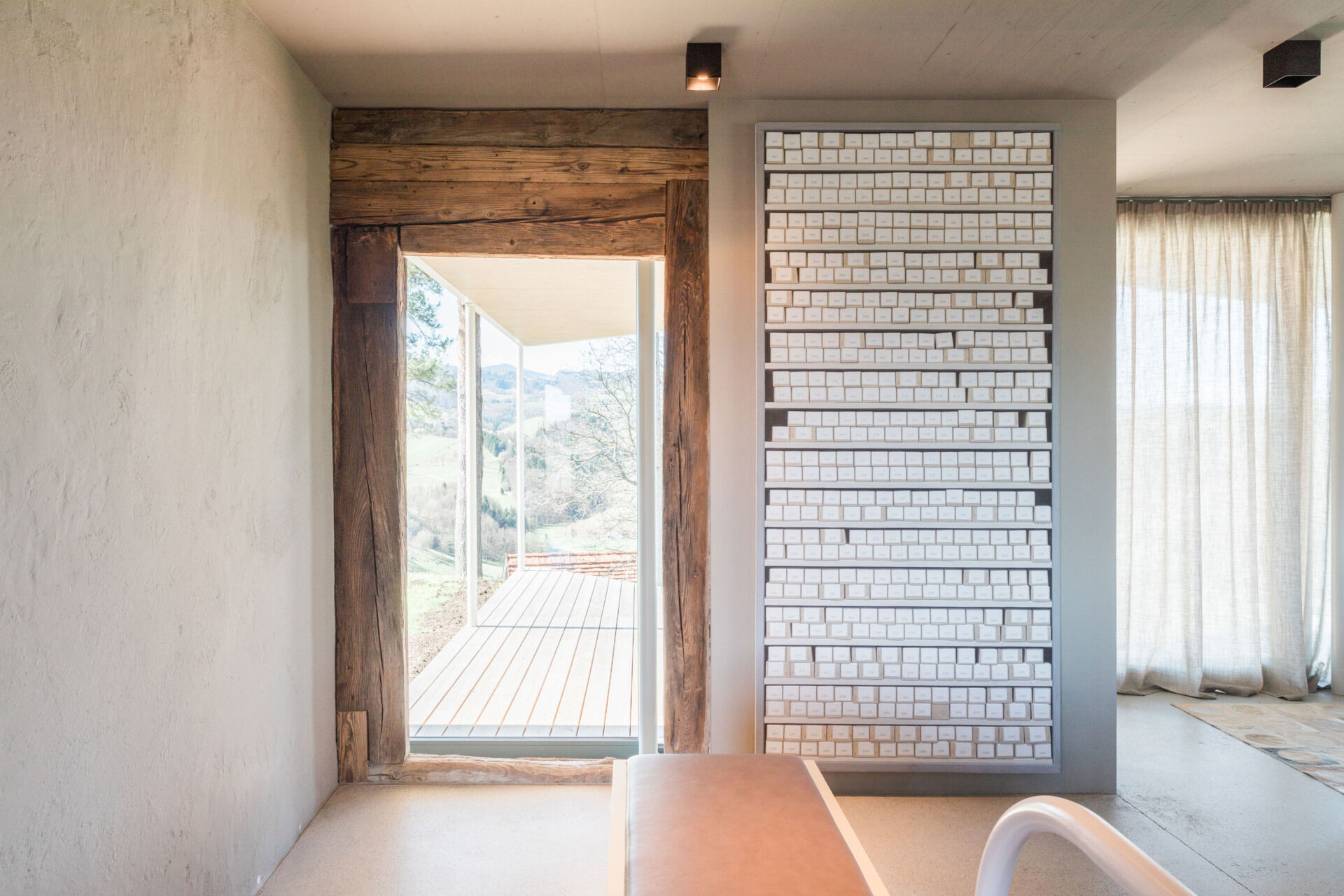 An Austrian farmhouse entryway combines weathered timber, a stone bench, linen curtains, and a modern interior with unusual architectural details.