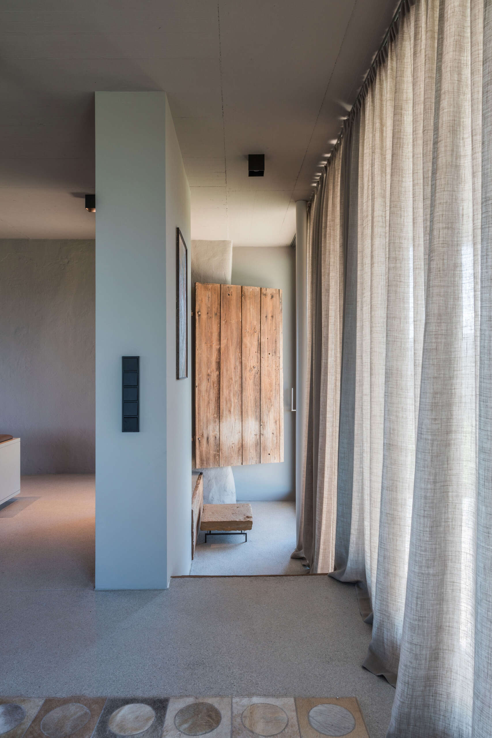 An Austrian farmhouse entryway combines weathered timber, a stone bench, linen curtains, and a modern interior with unusual architectural details.