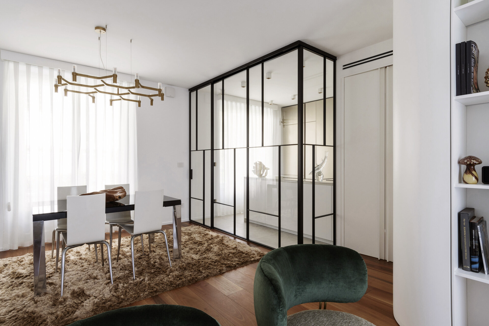 A glass-enclosed kitchen in a Turin apartment features floor-to-ceiling black metal frames, a sliding glass door, minimalist cabinetry, and marble-look countertops.