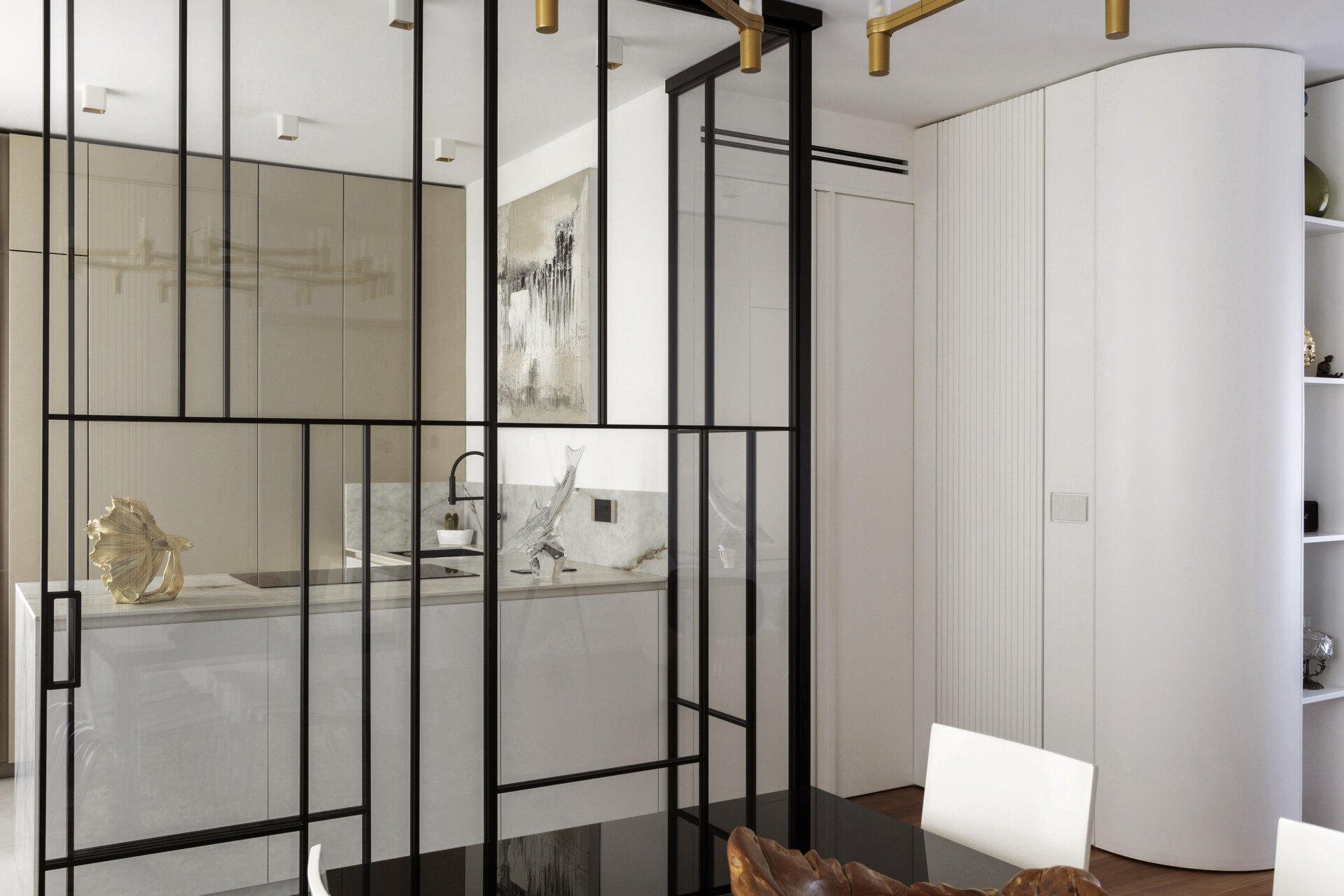 A glass-enclosed kitchen in a Turin apartment features floor-to-ceiling black metal frames, a sliding glass door, minimalist cabinetry, and marble-look countertops.