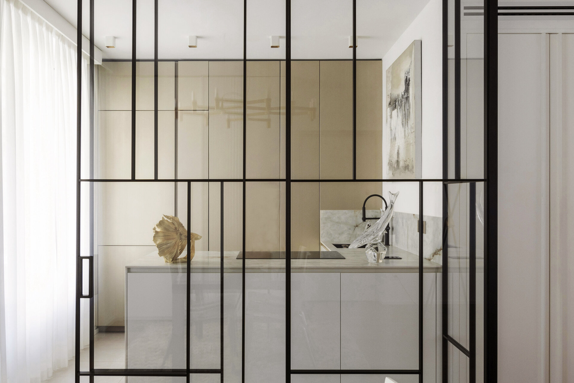 A glass-enclosed kitchen in a Turin apartment features floor-to-ceiling black metal frames, a sliding glass door, minimalist cabinetry, and marble-look countertops.