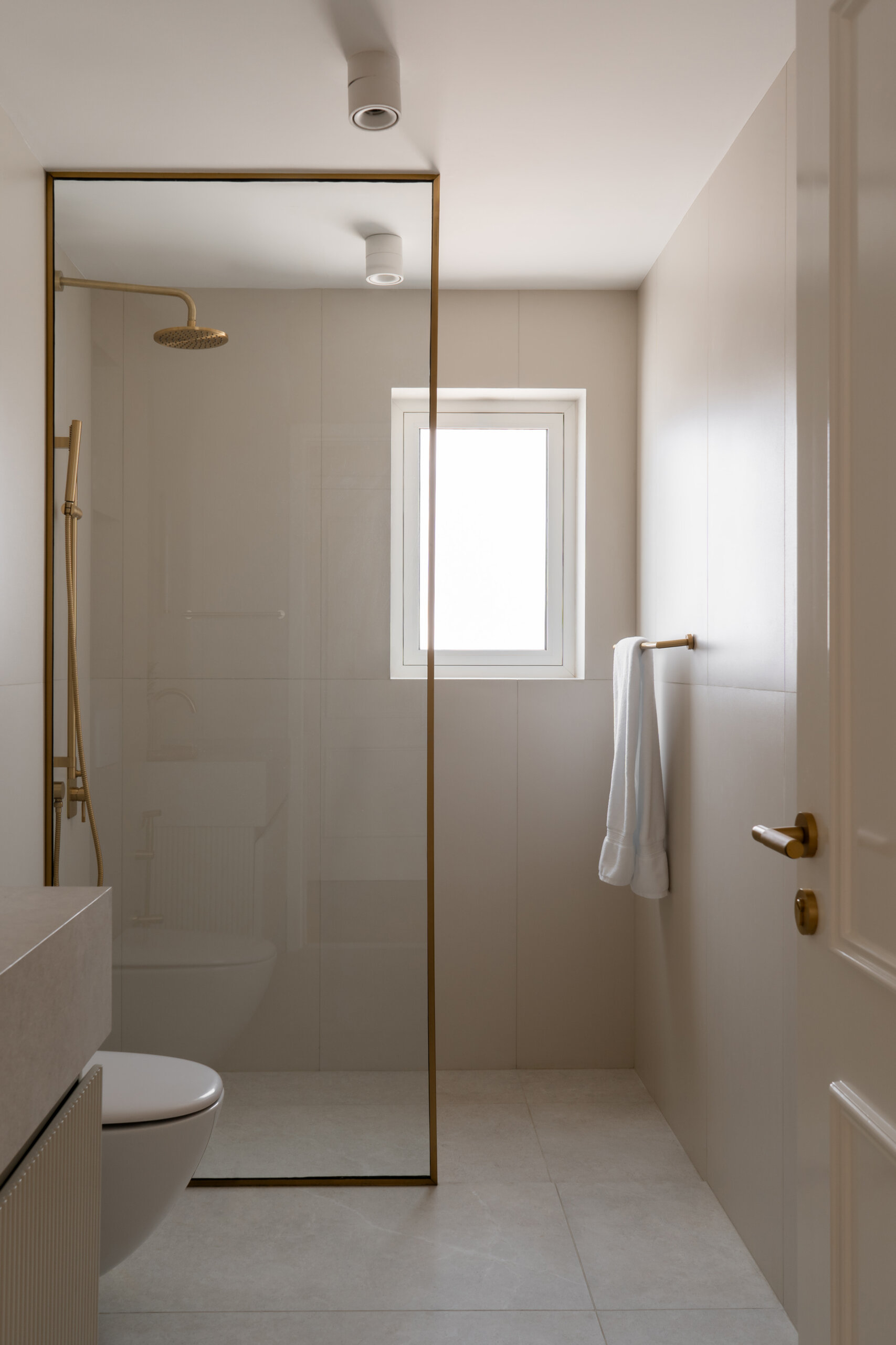 A contemporary guest bathroom in The White Arcade, Dubai, featuring a natural stone vanity with an integrated sink, arched brass-framed mirror, ribbed cabinetry, walk-in glass shower, and beautiful brass fixtures. Designed by D’Ora Tokai Designs.