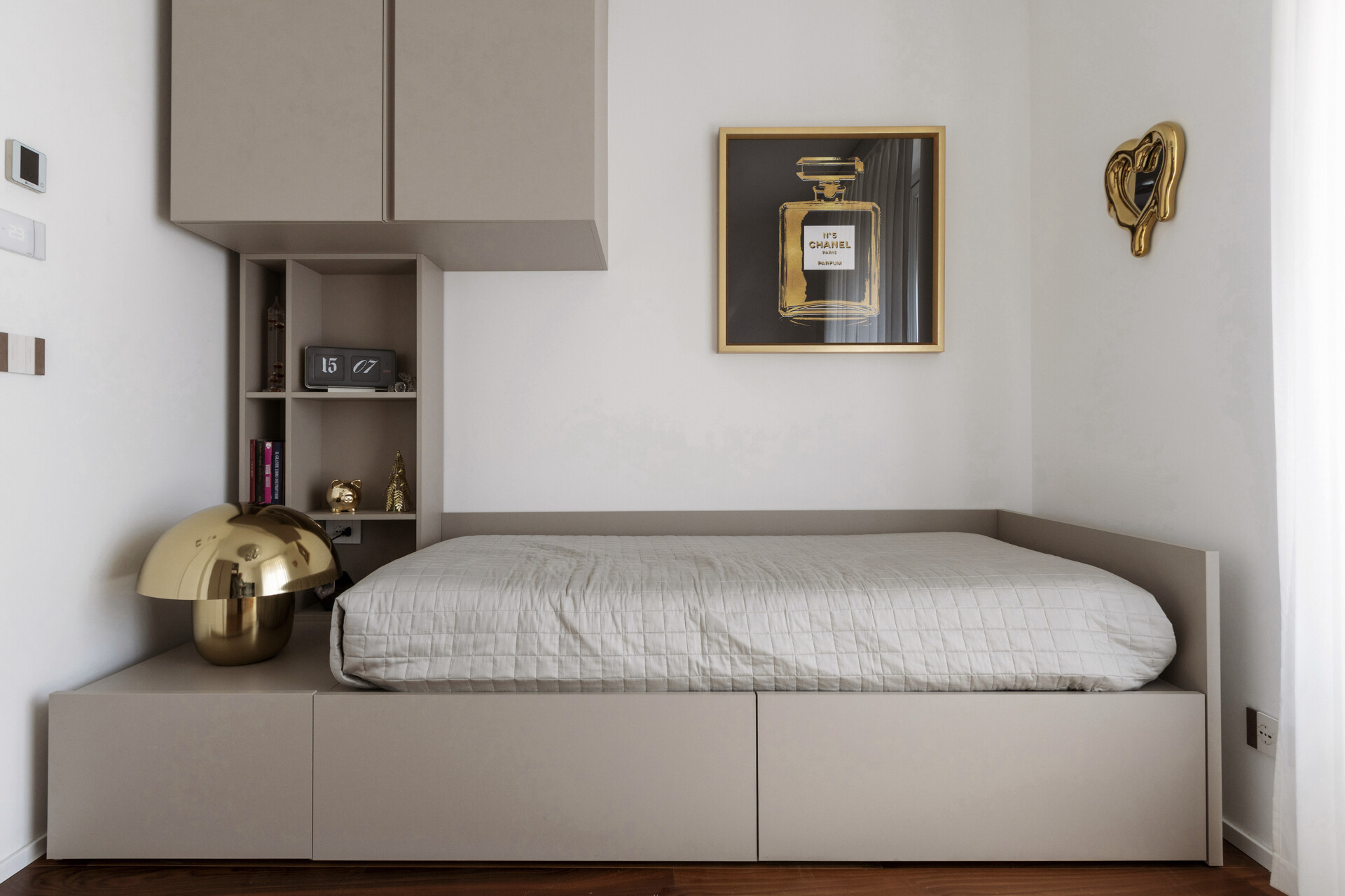 A compact guest bedroom features a single bed with built-in storage, overhead cabinets, a dedicated desk, open shelving, and a pink upholstered chair.