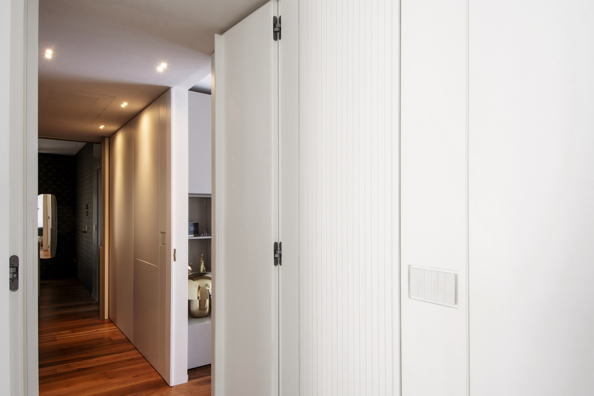 Curved white cabinetry conceals a hallway entrance in this Italian apartment, with flush doors, integrated storage, and custom wall panelling.