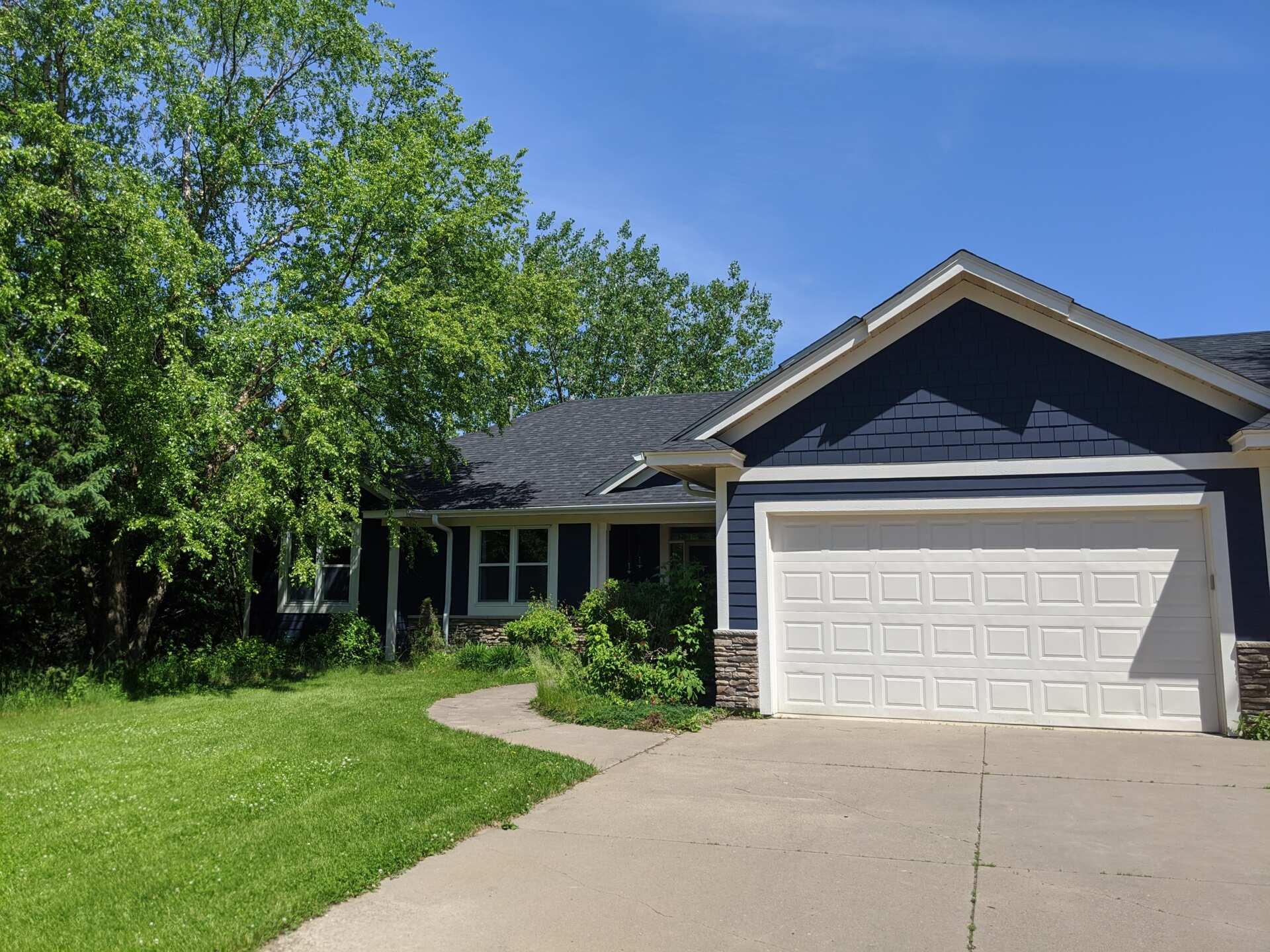 The original 1990s house before its modern renovation, featuring blue siding, white trim, a pitched roof, and an attached two-car garage surrounded by mature trees.