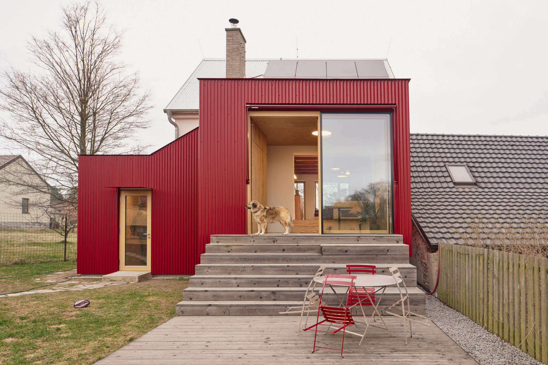 A large sliding window opens this Czech home by Facha architekti onto a larch terrace with wide seating steps and a retractable textile awning, creating an easy transition between the renovated interior and garden.
