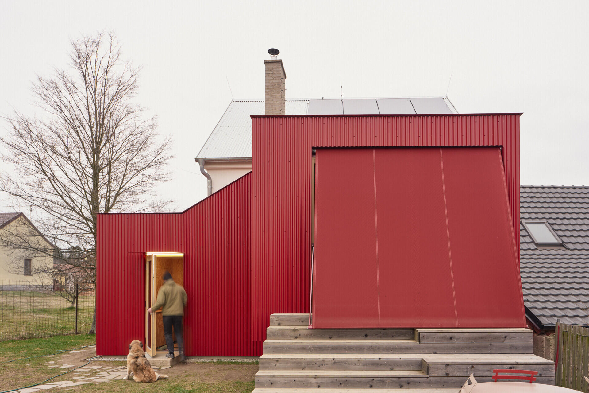 A large sliding window opens this Czech home by Facha architekti onto a larch terrace with wide seating steps and a retractable textile awning, creating an easy transition between the renovated interior and garden.