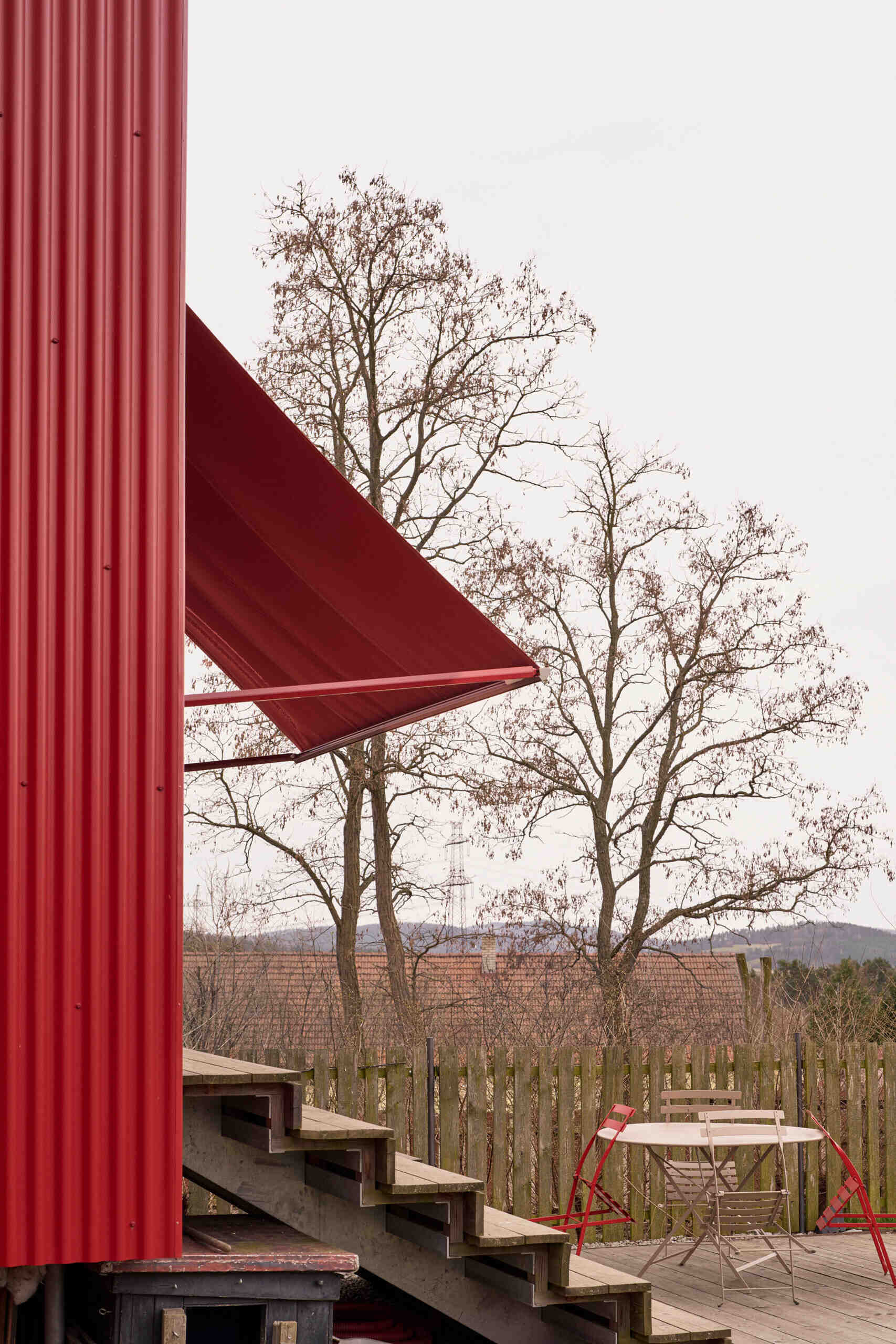 A large sliding window opens this Czech home by Facha architekti onto a larch terrace with wide seating steps and a retractable textile awning, creating an easy transition between the renovated interior and garden.