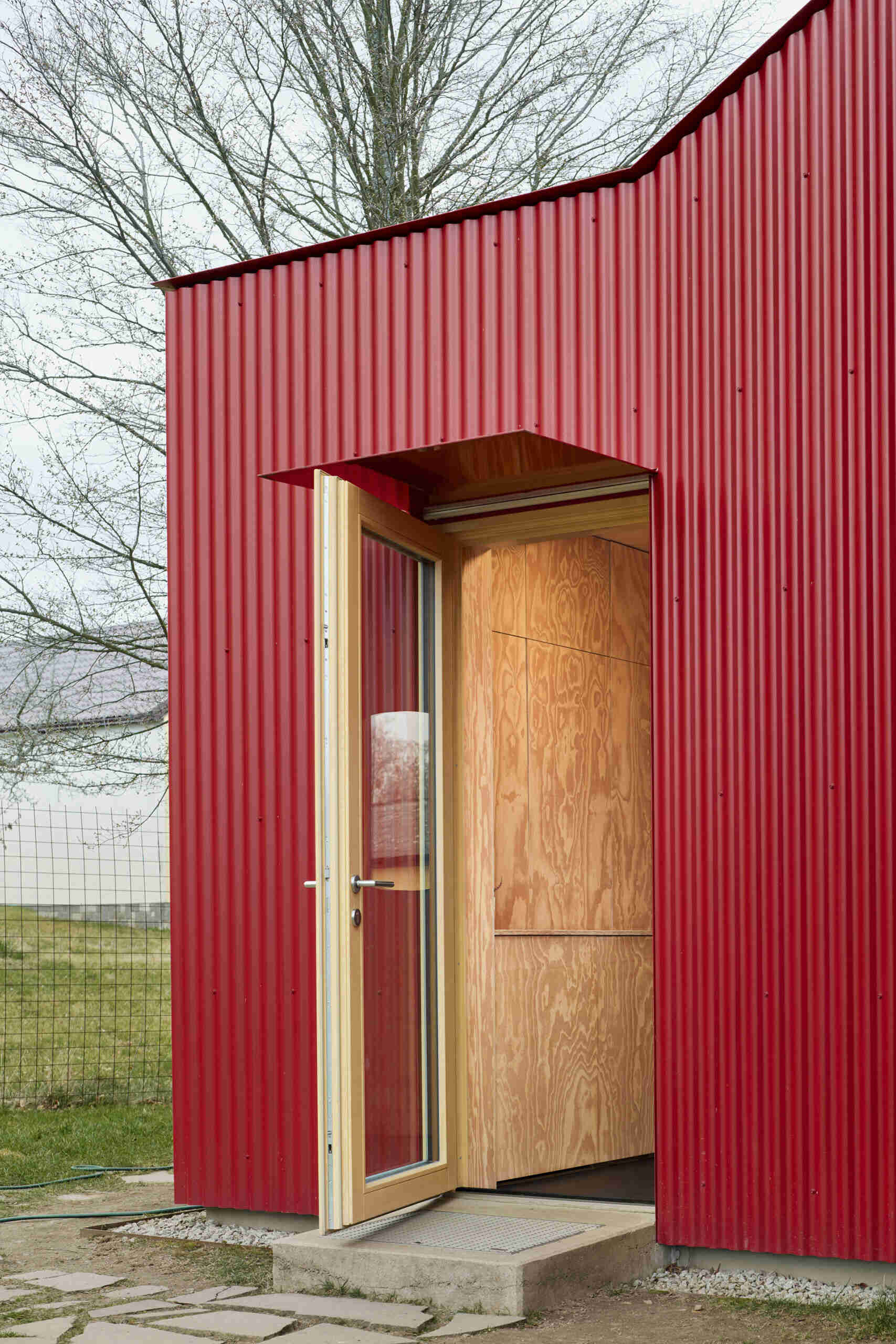 The relocated entrance to this home in Ne?ín, Czech Republic, is set into the new red corrugated metal extension by Facha architekti. Moving the doorway helped reorganise the interior while pine plywood brings warmth to the space inside.