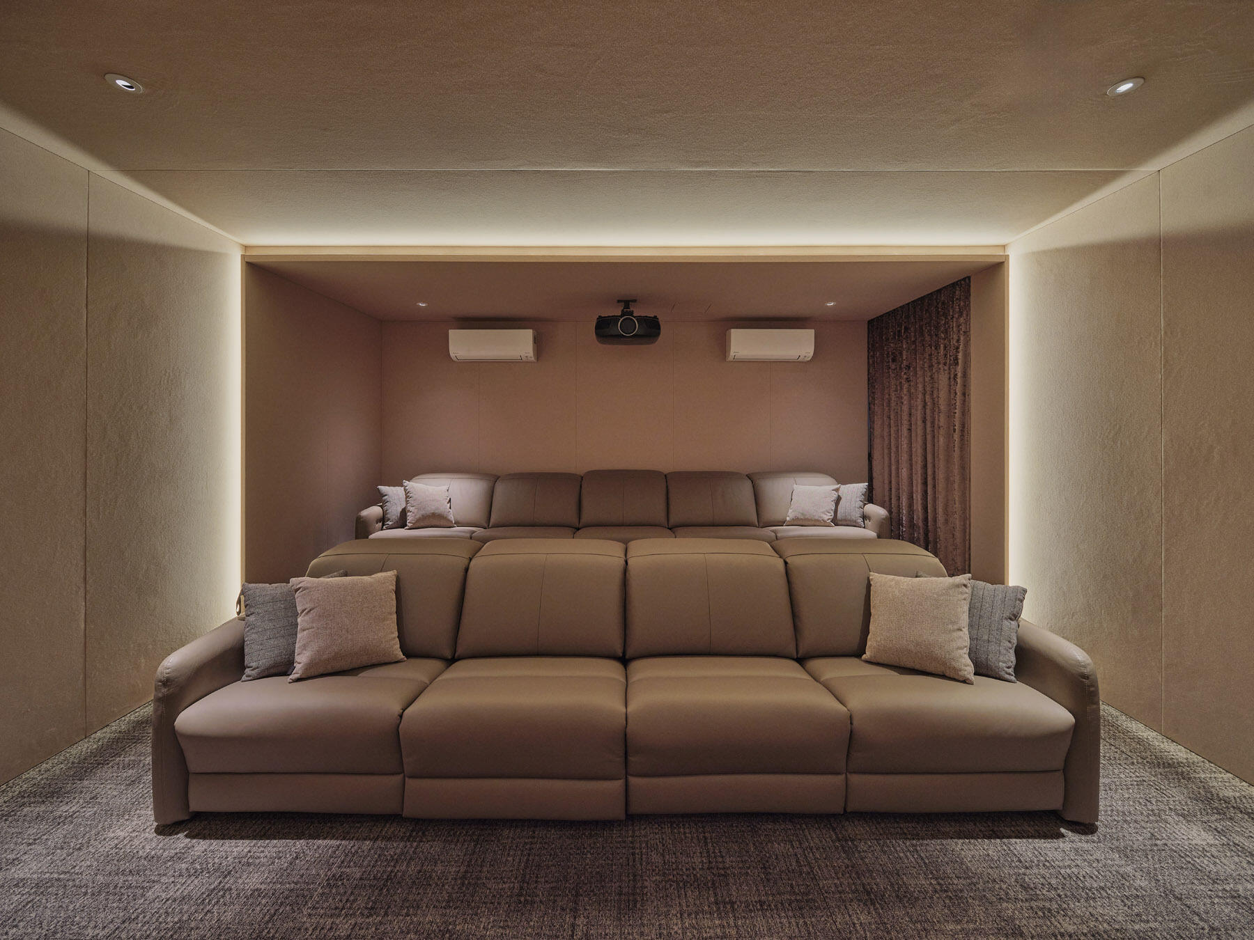 Look inside the private home cinema at JS-House, featuring stepped seating, comfortable upholstered sofas, soft carpeting, blackout curtains, and subtle integrated lighting.