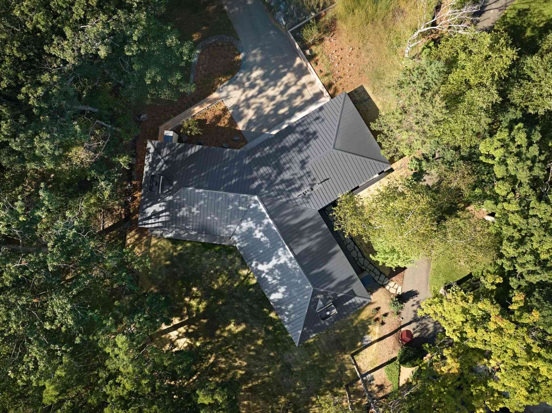 An aerial view of a modern Y-shaped house in Minnesota, showing its three wings, dark metal roof, and surrounding woodland. The unusual architectural layout was inspired by a neighboring Frank Lloyd Wright design.