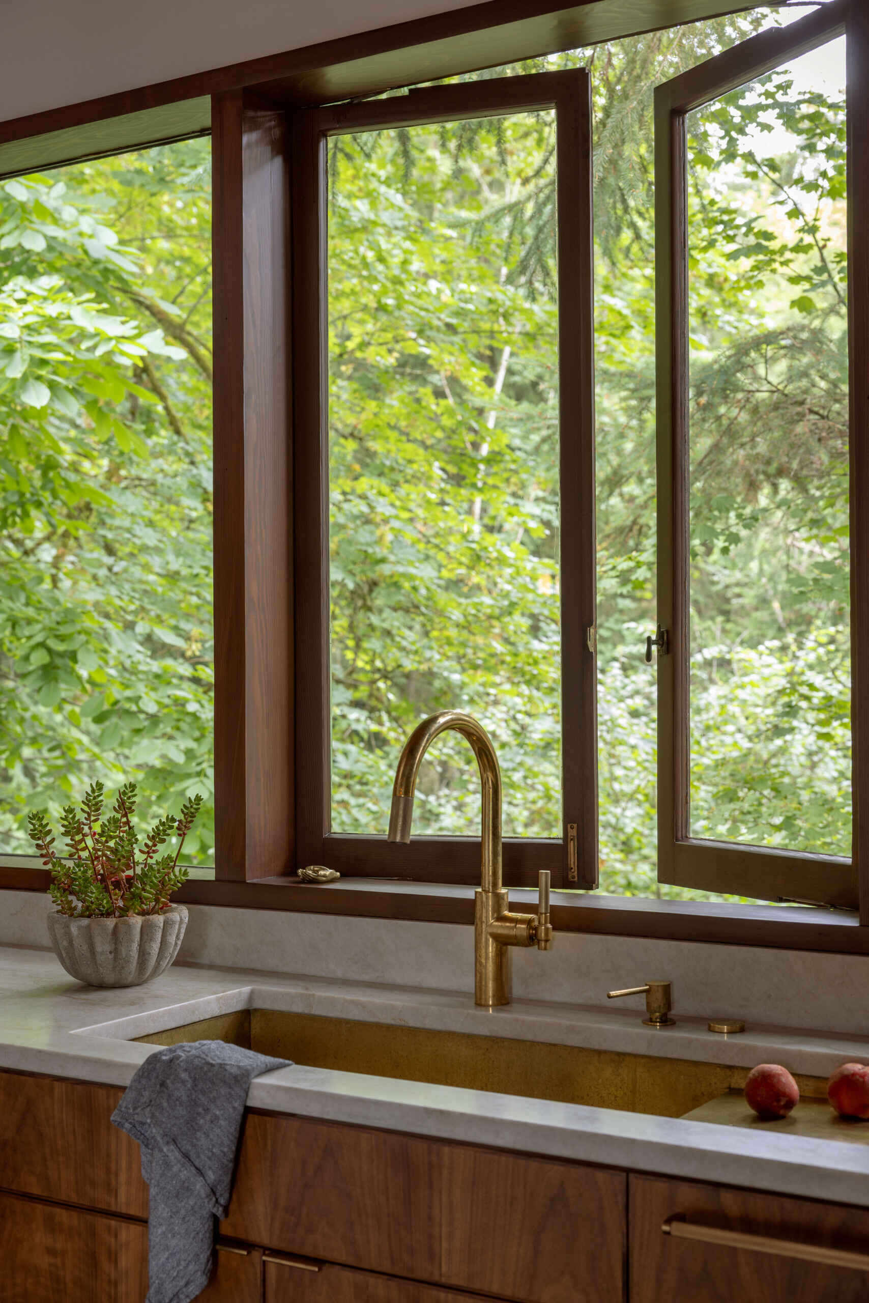 Explore the renovated kitchen of The Burrows, a mid-century modern home in Seattle by chadbourne + doss architects. Custom walnut cabinetry, slatted wood details, brass fixtures, pale stone countertops, a brass chef's sink, and a sculptural kitchen island bring warmth and functionality to the space.