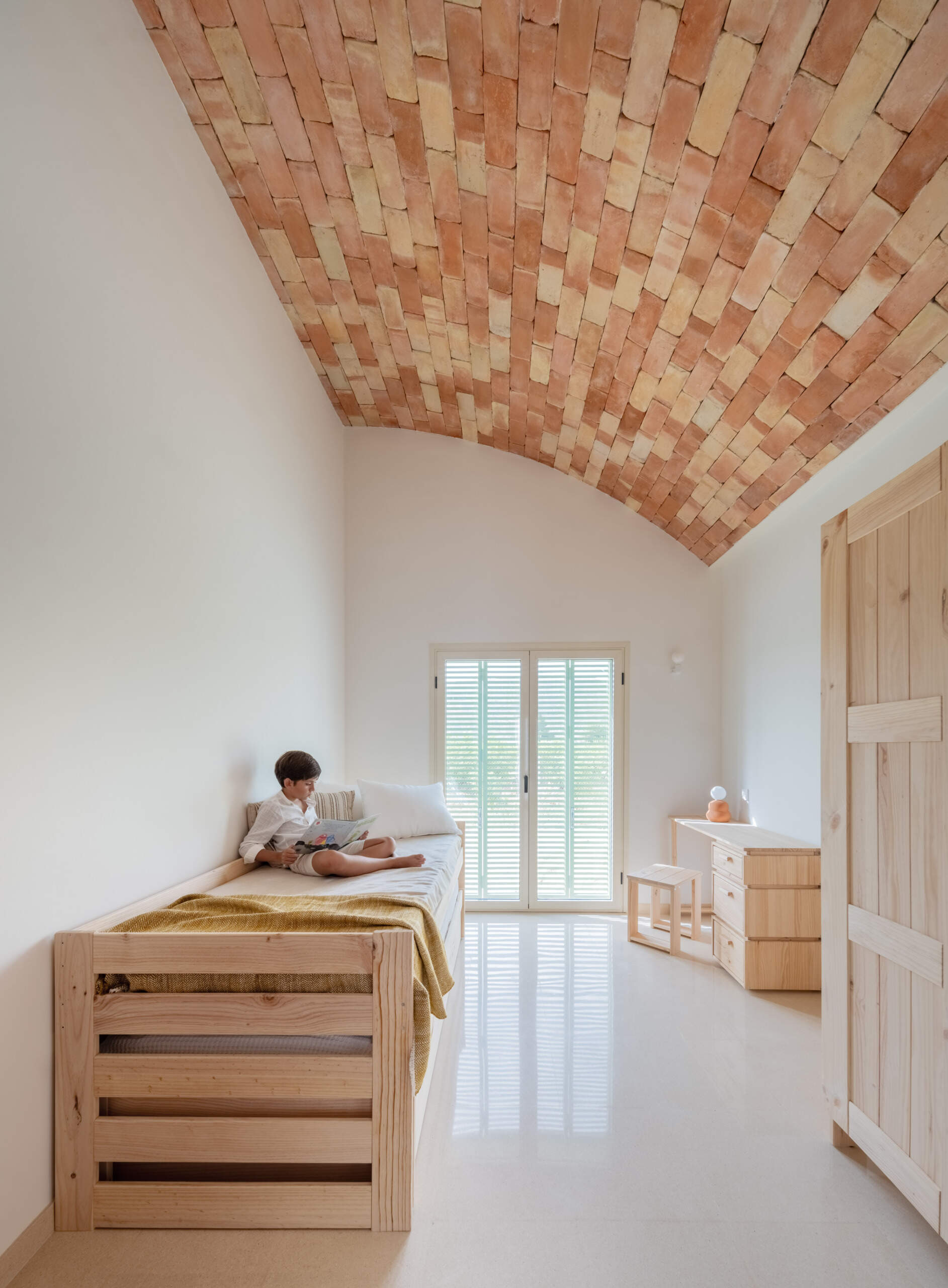 Explore the minimalist bedrooms at Casa Vereda in Spain, featuring curved brick ceilings, natural pine furniture, pale terrazzo floors, and Mediterranean shutters. Simple bedroom interiors with warm materials and contemporary Spanish design.