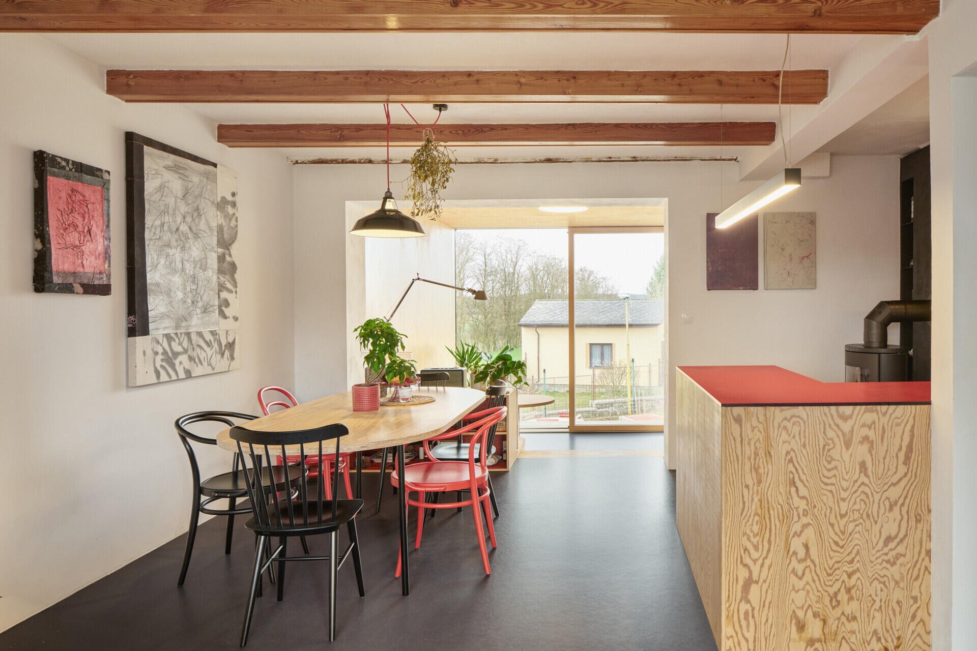 The redesigned kitchen and dining area in this Ne?ín home by Facha architekti combines custom pine plywood cabinetry, natural linoleum flooring and a rotating wood-burning stove within the reworked ground floor.