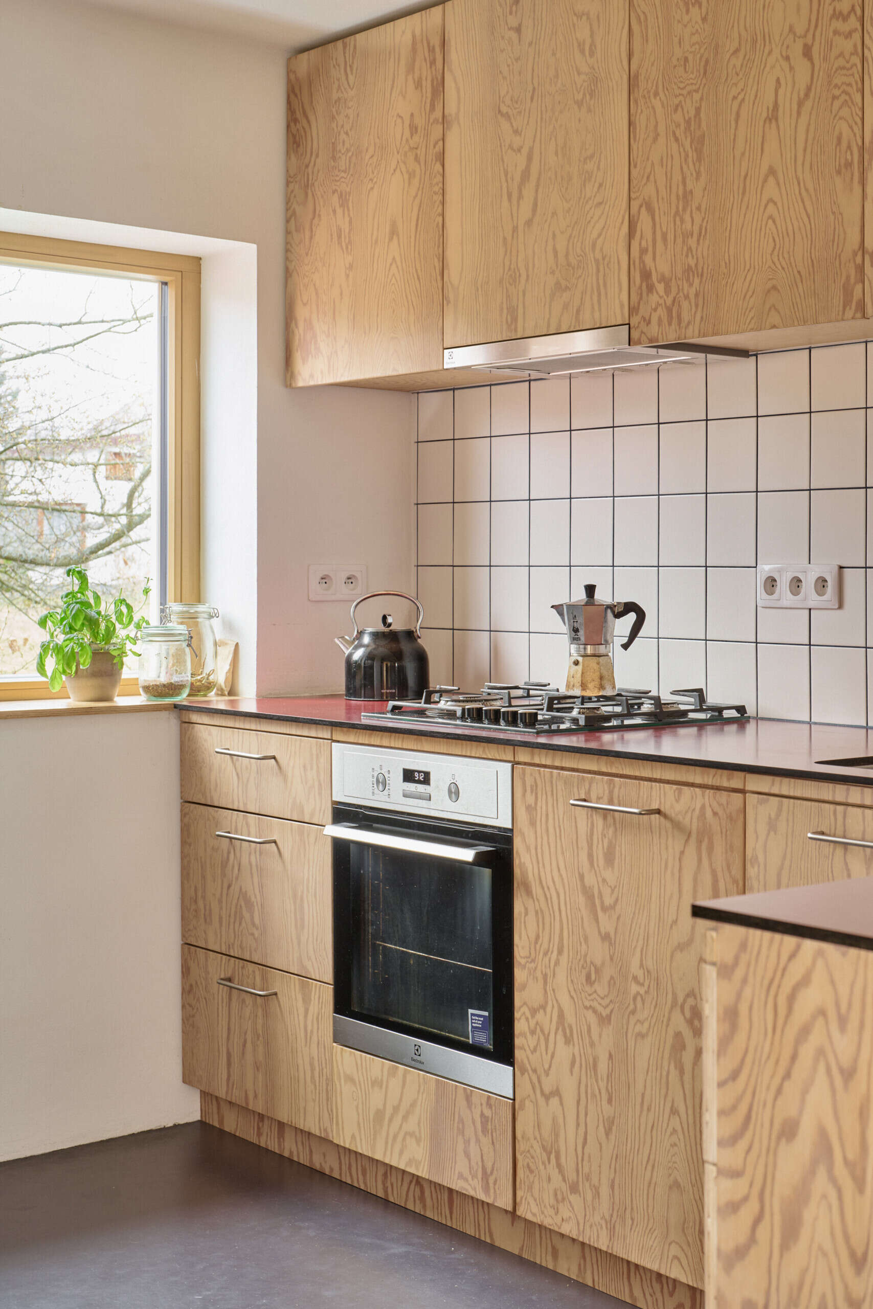 The redesigned kitchen and dining area in this Ne?ín home by Facha architekti combines custom pine plywood cabinetry, natural linoleum flooring and a rotating wood-burning stove within the reworked ground floor.