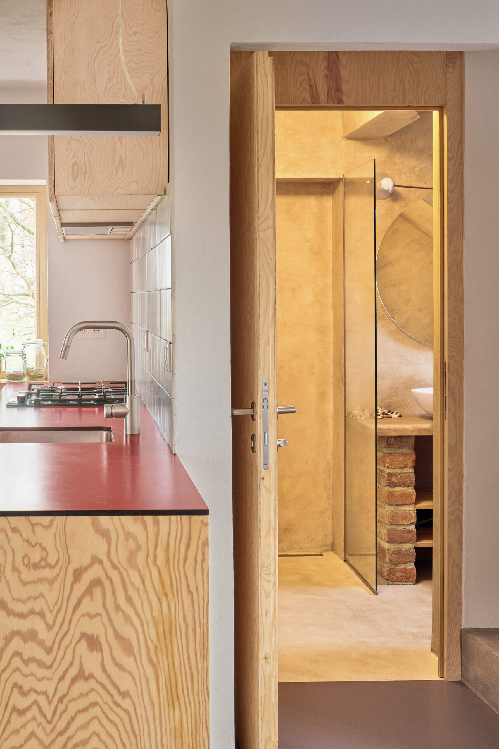 The enlarged bathroom in this Ne?ín home by Facha architekti is finished in cement-based plaster, with a frameless glass shower and timber details creating a compact space with a simple, tactile material palette.