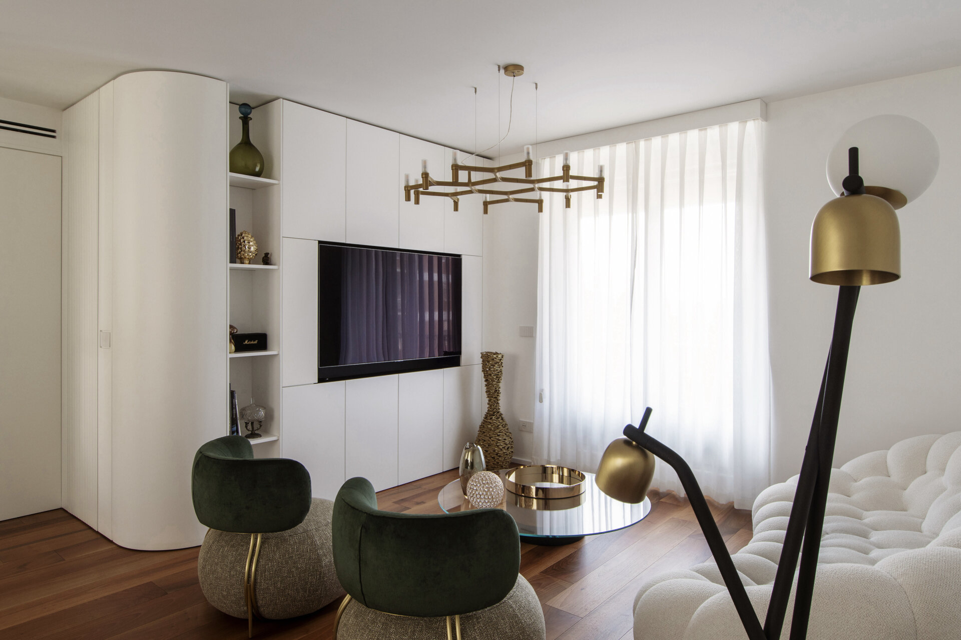 This contemporary living room features curved white built-in cabinetry, a Roche Bobois Bubble sofa, green velvet armchairs, brass lighting, and walnut parquet flooring.