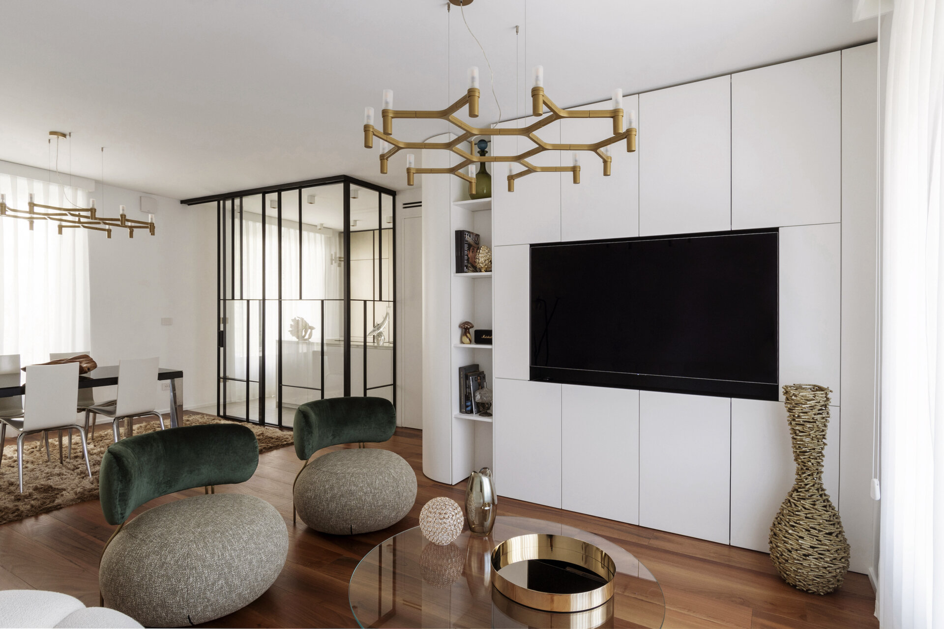 This contemporary living room features curved white built-in cabinetry, a Roche Bobois Bubble sofa, green velvet armchairs, brass lighting, and walnut parquet flooring.