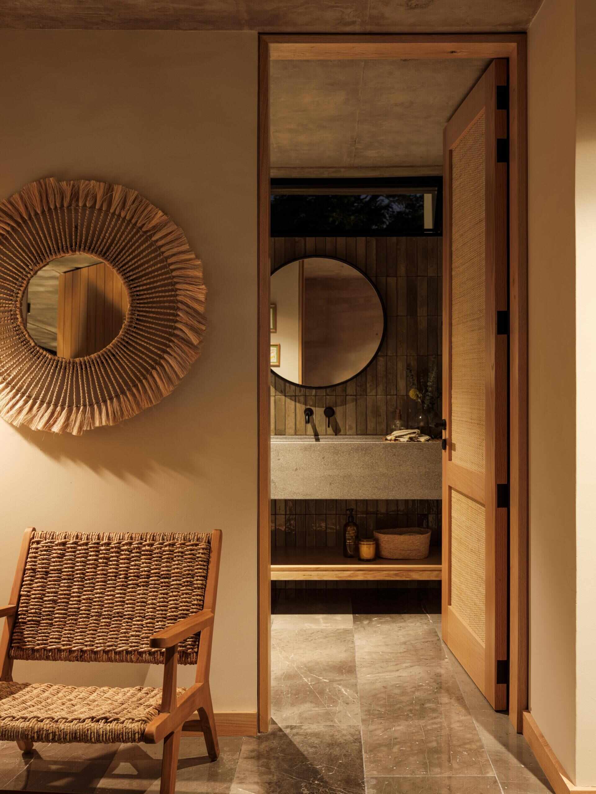 Explore a modern bathroom featuring earthy vertical tiles, a stone vanity with an integrated sink, matte black fixtures, a round mirror, and warm wood details. A beautiful example of natural materials in contemporary bathroom design.