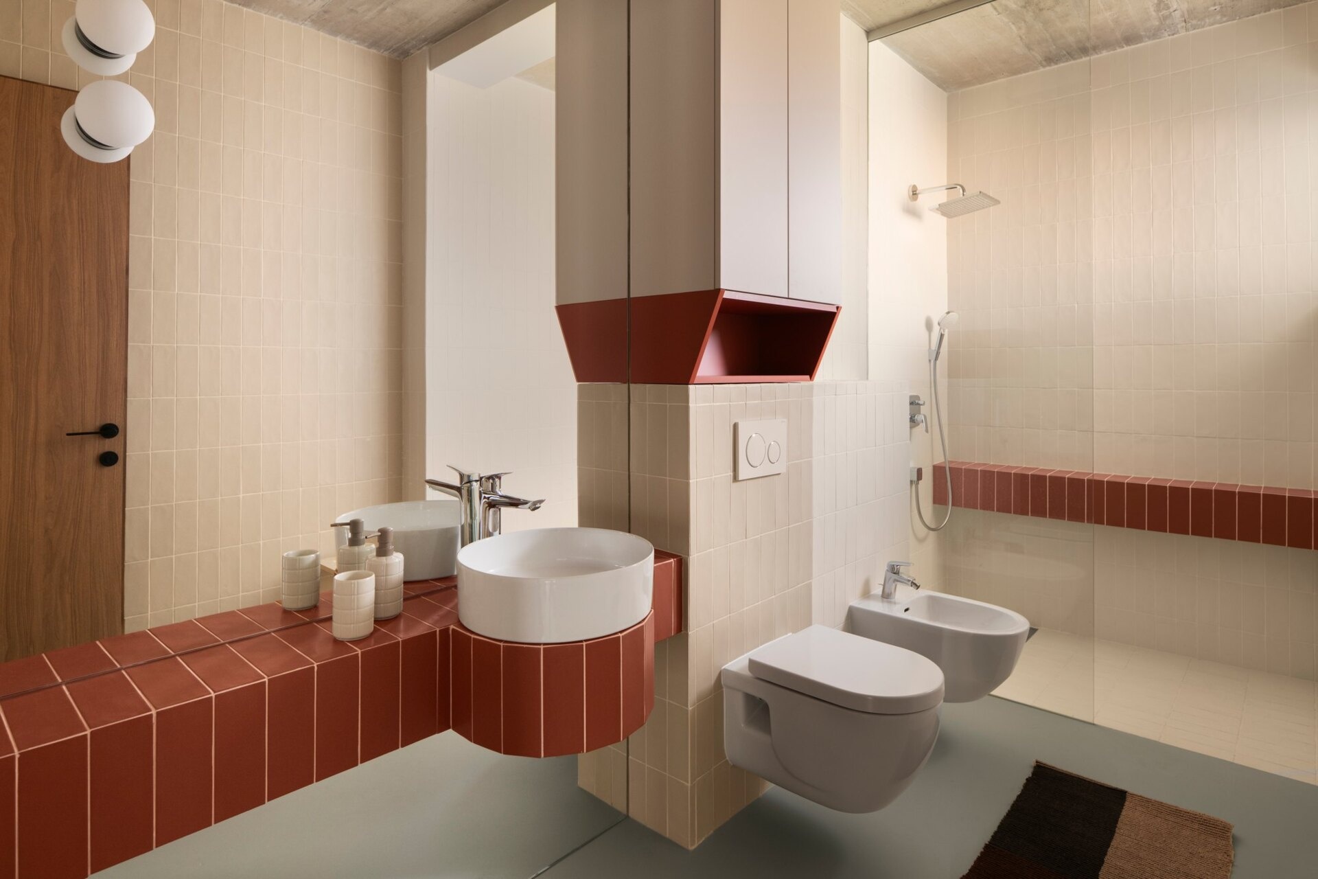 Discover the bathrooms at Arc House in Croatia, featuring rust-red tiled vanities, curved sink surrounds, cream wall tiles, white vessel basins, walk-in showers and exposed concrete ceilings.