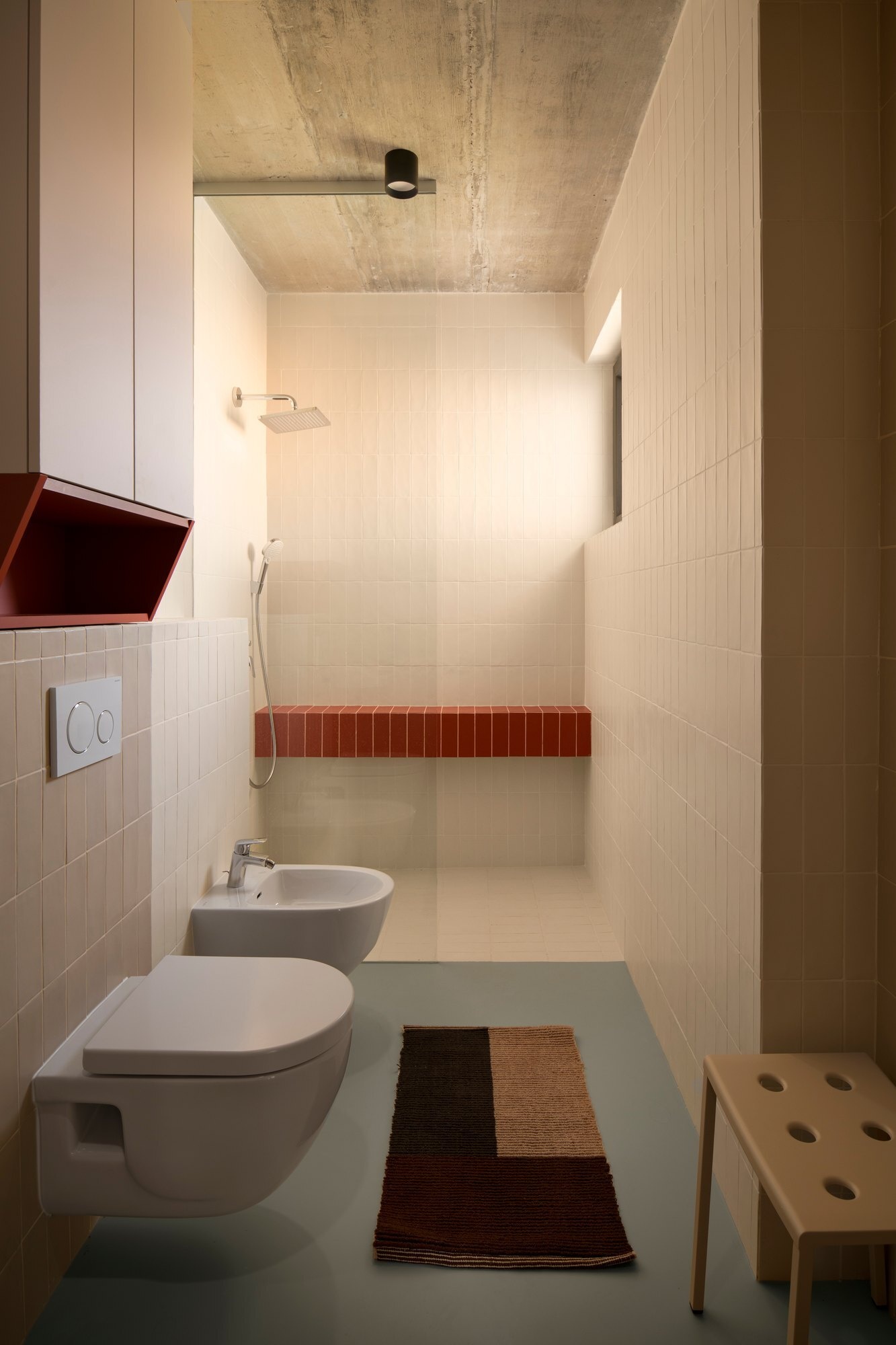 Discover the bathrooms at Arc House in Croatia, featuring rust-red tiled vanities, curved sink surrounds, cream wall tiles, white vessel basins, walk-in showers and exposed concrete ceilings.