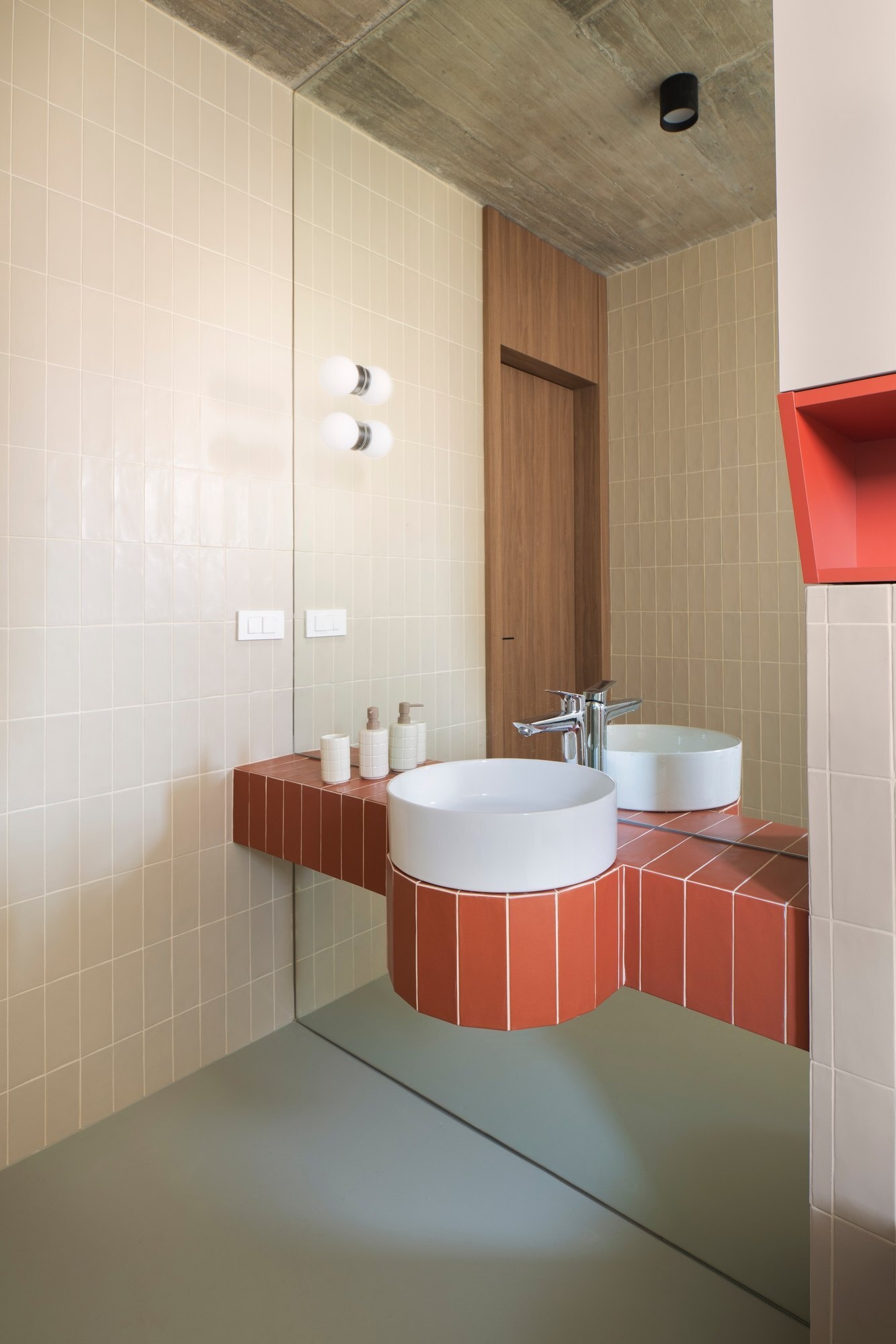 Discover the bathrooms at Arc House in Croatia, featuring rust-red tiled vanities, curved sink surrounds, cream wall tiles, white vessel basins, walk-in showers and exposed concrete ceilings.