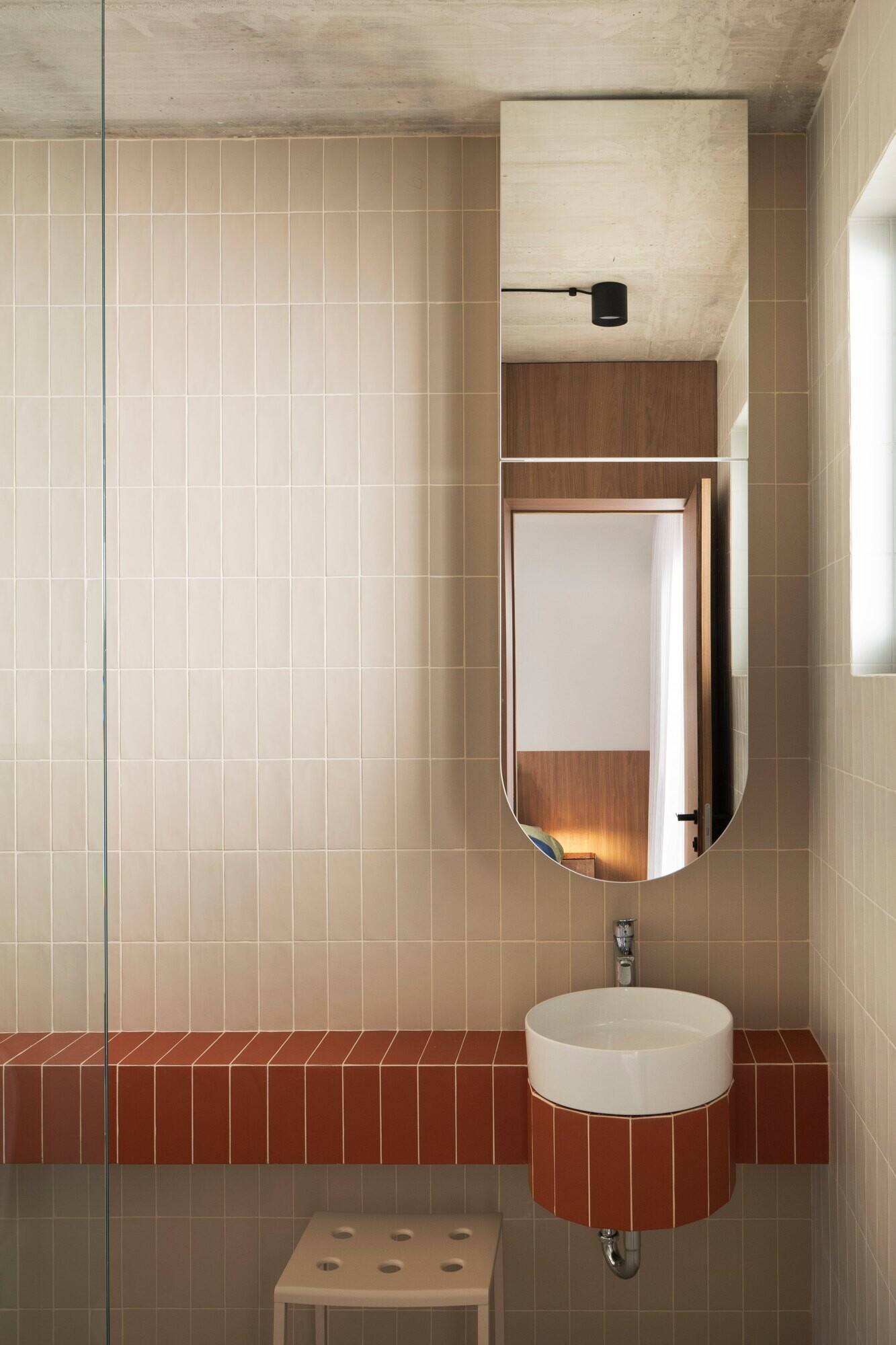 Discover the bathrooms at Arc House in Croatia, featuring rust-red tiled vanities, curved sink surrounds, cream wall tiles, white vessel basins, walk-in showers and exposed concrete ceilings.