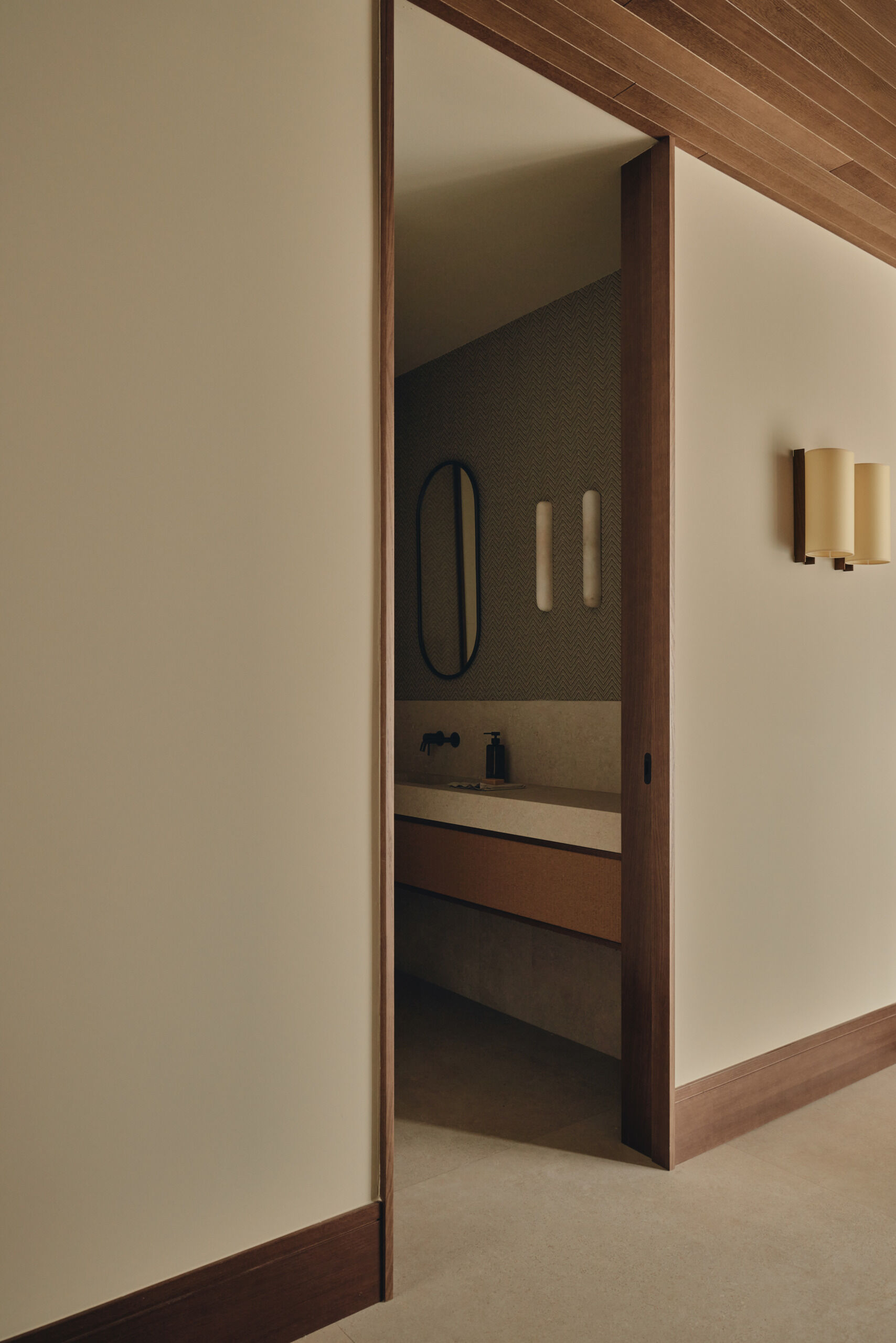 Discover minimalist modern bathrooms with pale stone-look vanities, integrated sinks, oval mirrors, matte black faucets, natural woven cabinetry, and large windows overlooking greenery.