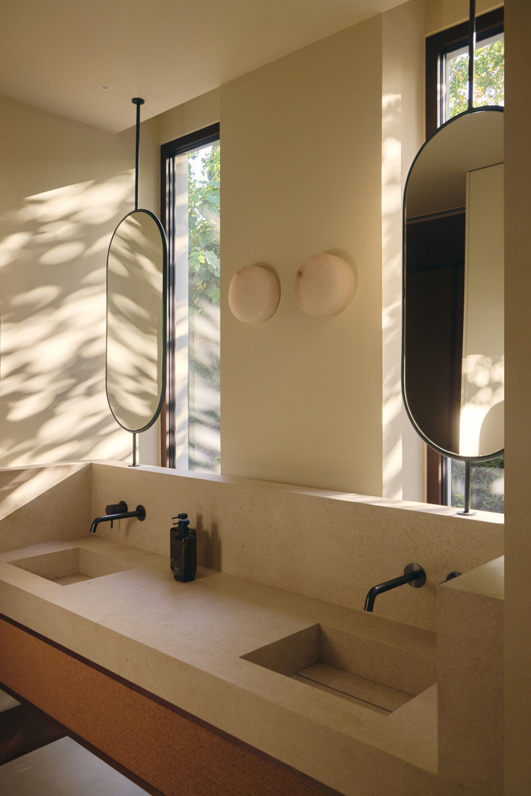 Discover minimalist modern bathrooms with pale stone-look vanities, integrated sinks, oval mirrors, matte black faucets, natural woven cabinetry, and large windows overlooking greenery.