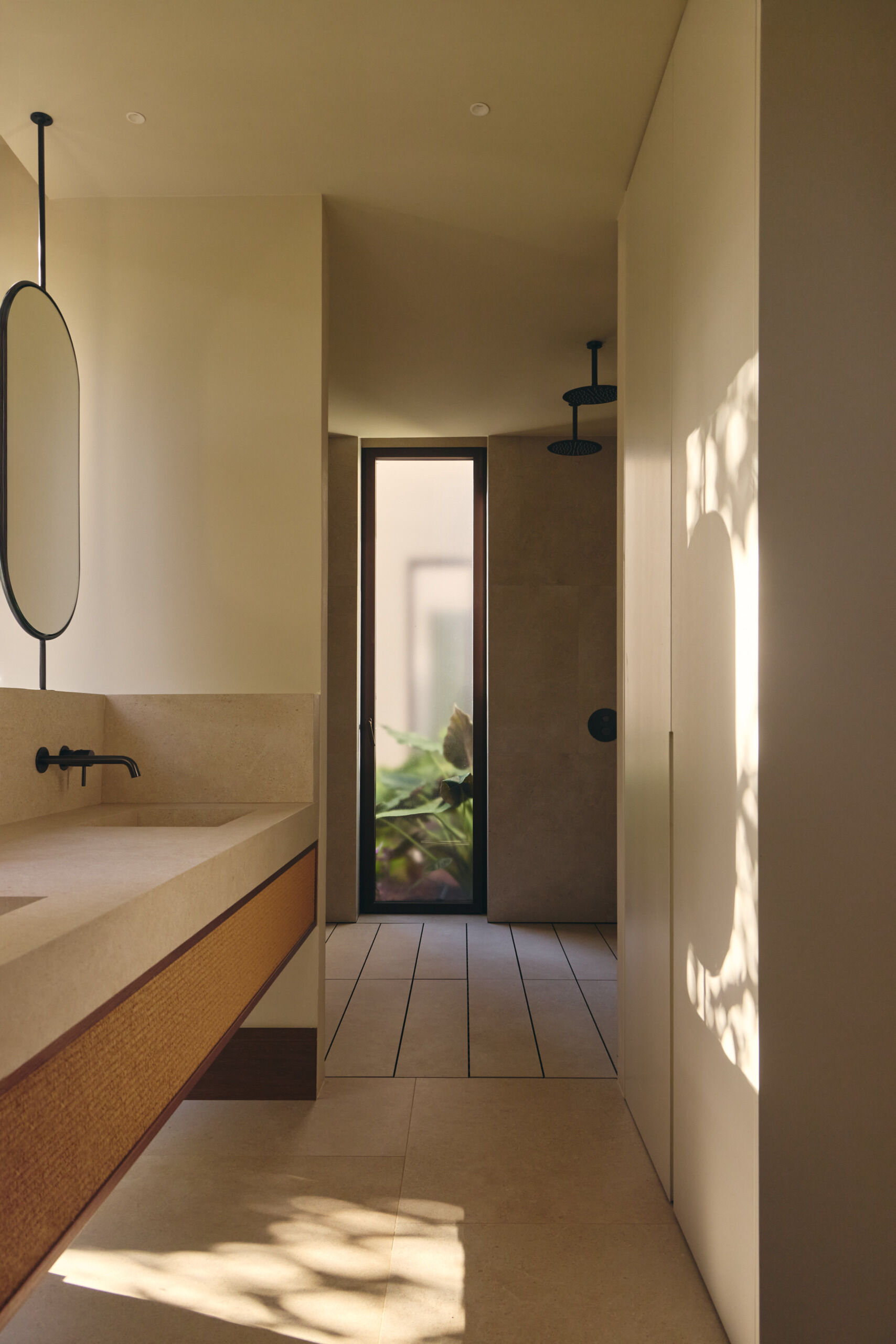 Discover minimalist modern bathrooms with pale stone-look vanities, integrated sinks, oval mirrors, matte black faucets, natural woven cabinetry, and large windows overlooking greenery.