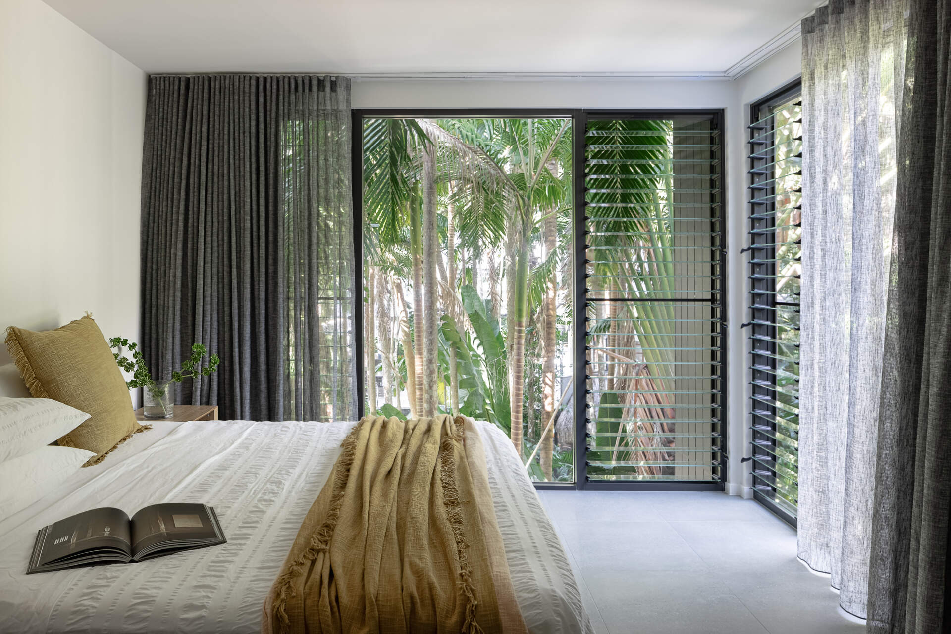 Discover the bedrooms at Raintree in Noosa Heads, Australia, designed by Void Building Design. Floor-to-ceiling rainforest views, charcoal curtains, neutral interiors, and soft bedroom textiles create a relaxing coastal atmosphere.