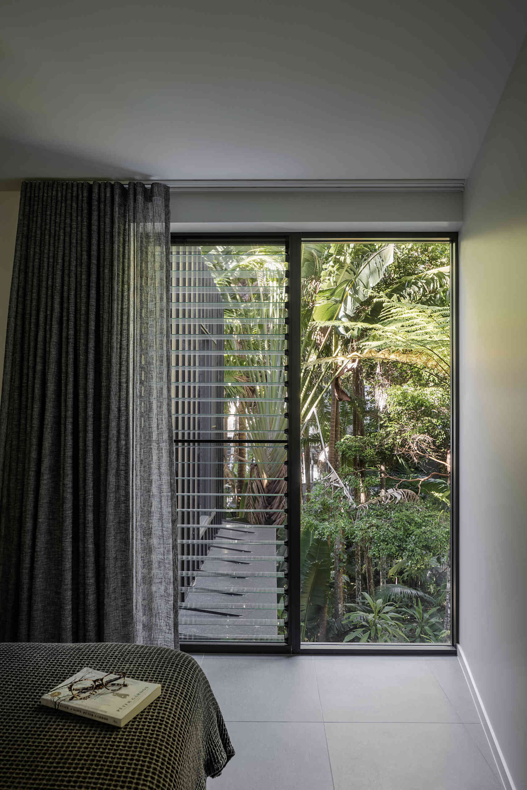 Discover the bedrooms at Raintree in Noosa Heads, Australia, designed by Void Building Design. Floor-to-ceiling rainforest views, charcoal curtains, neutral interiors, and soft bedroom textiles create a relaxing coastal atmosphere.