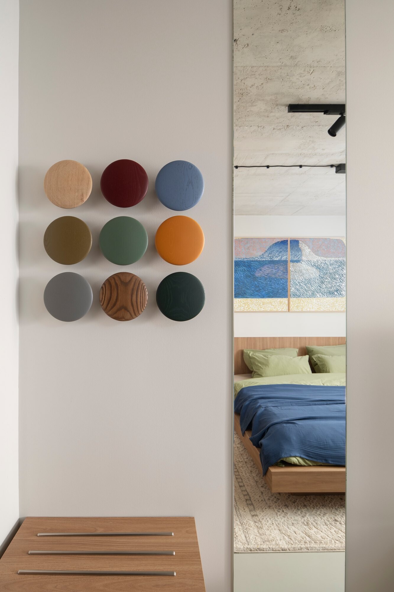 Explore a guest bedroom at Arc House in Istria, Croatia, with a minimalist timber headboard, built-in cabinetry, symmetrical black bedside lamps, blue bedding and colourful two-panel wall art.